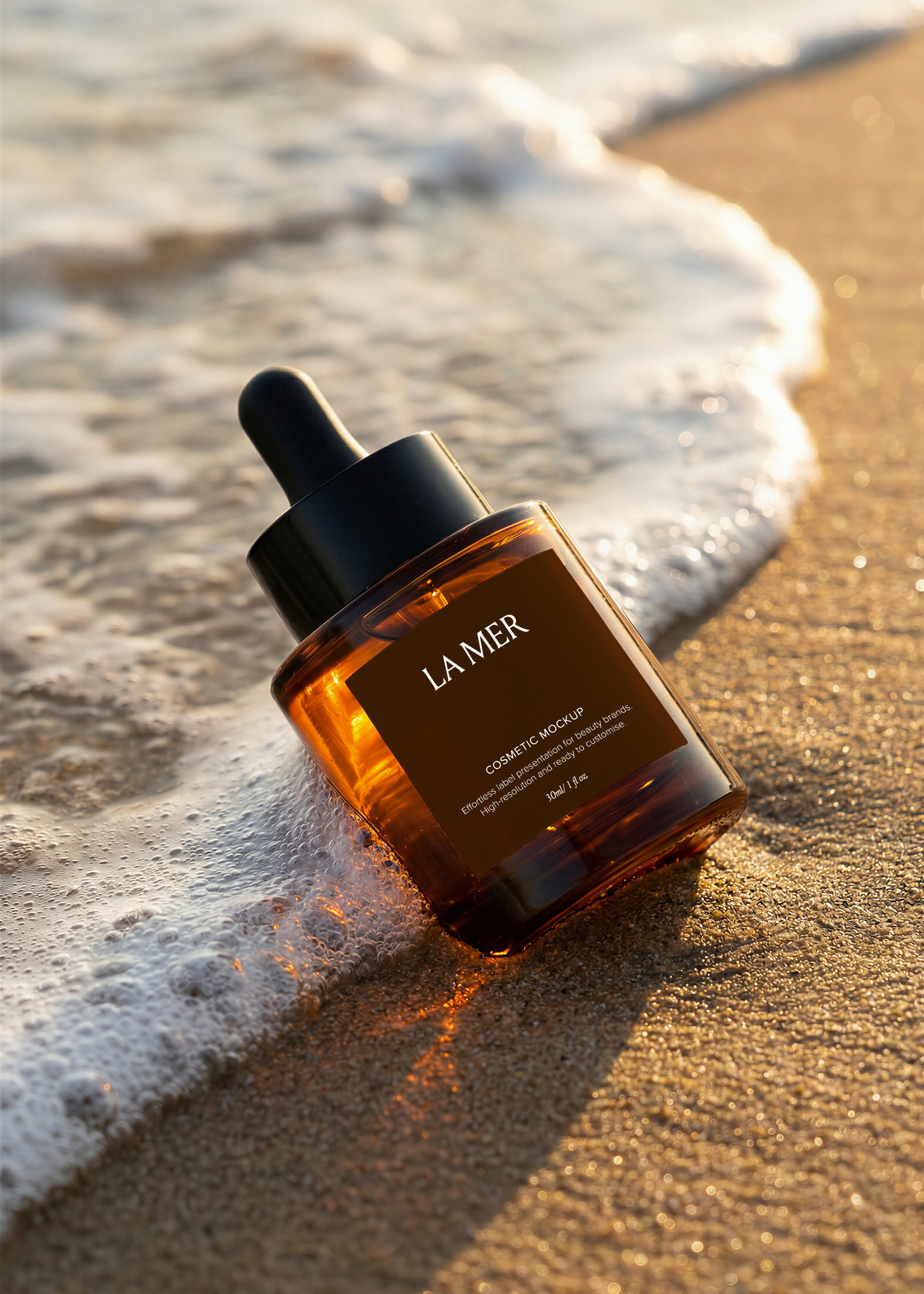 Amber dropper bottle mockup on wet sand at the water's edge with sea foam around it, backlit by golden-hour sunlight