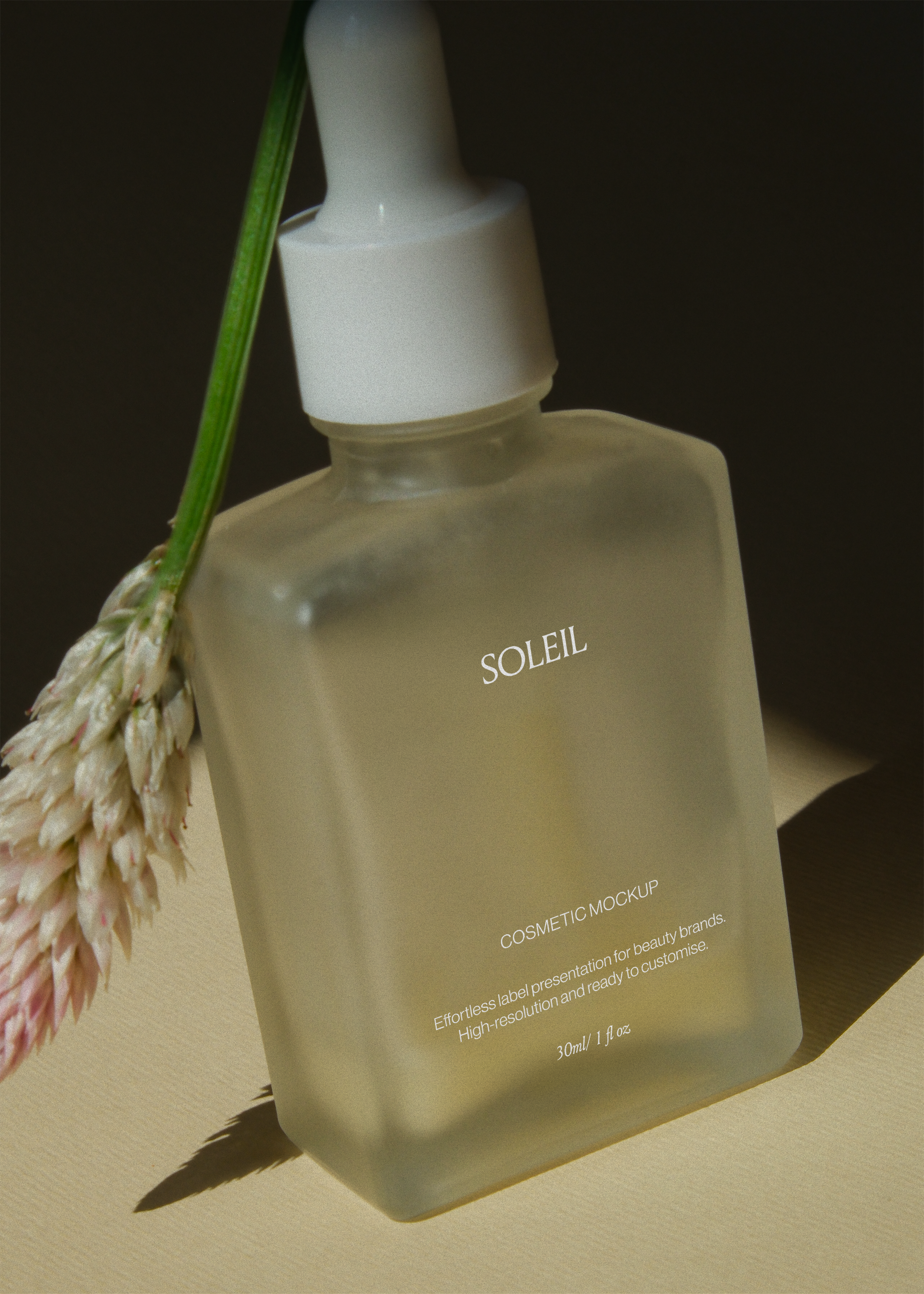 Frosted glass dropper bottle mockup angled against dried grass stem, dark backdrop, warm directional light