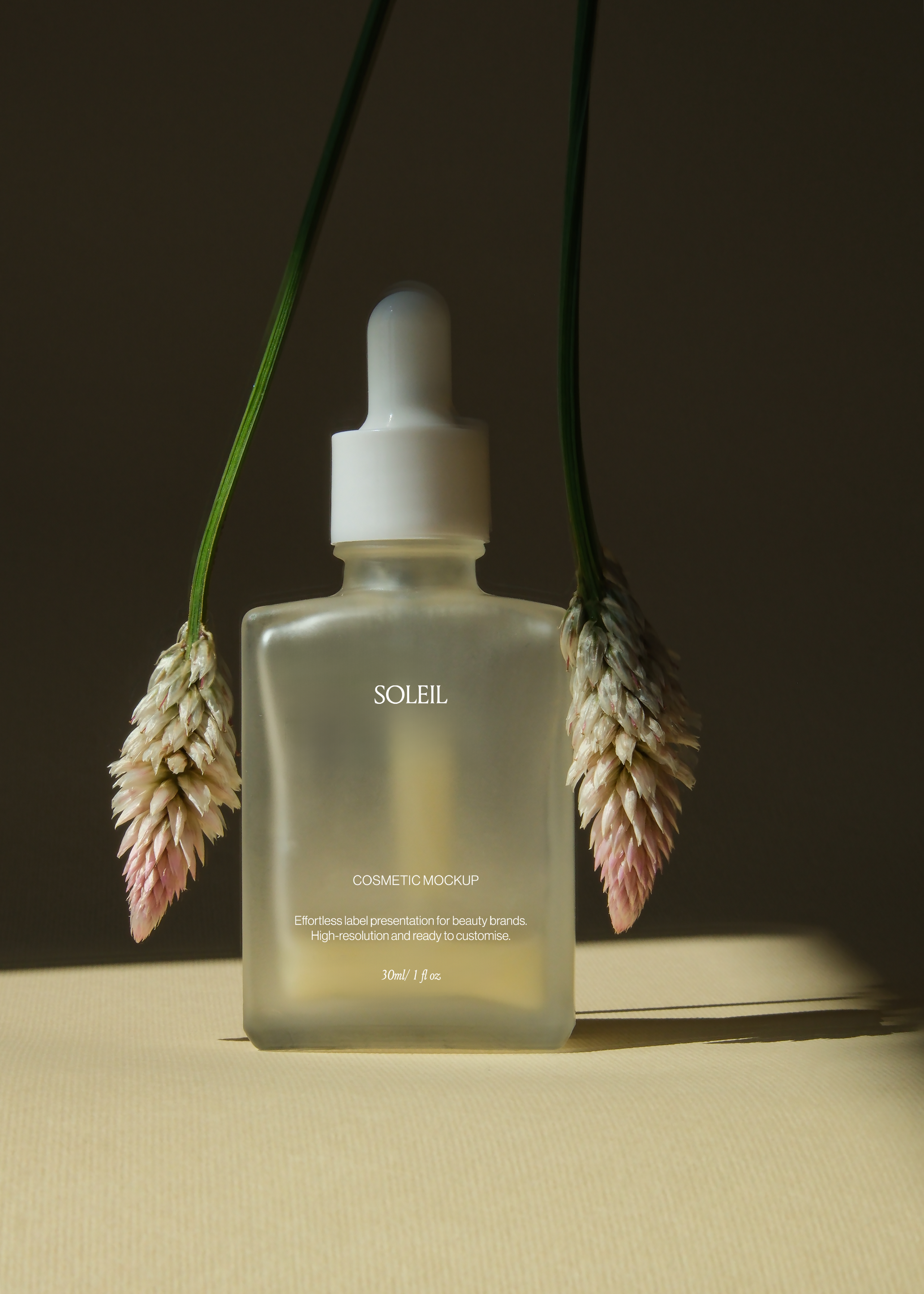 Frosted glass dropper bottle mockup framed symmetrically between two hanging dried grass heads, dark backdrop, warm light