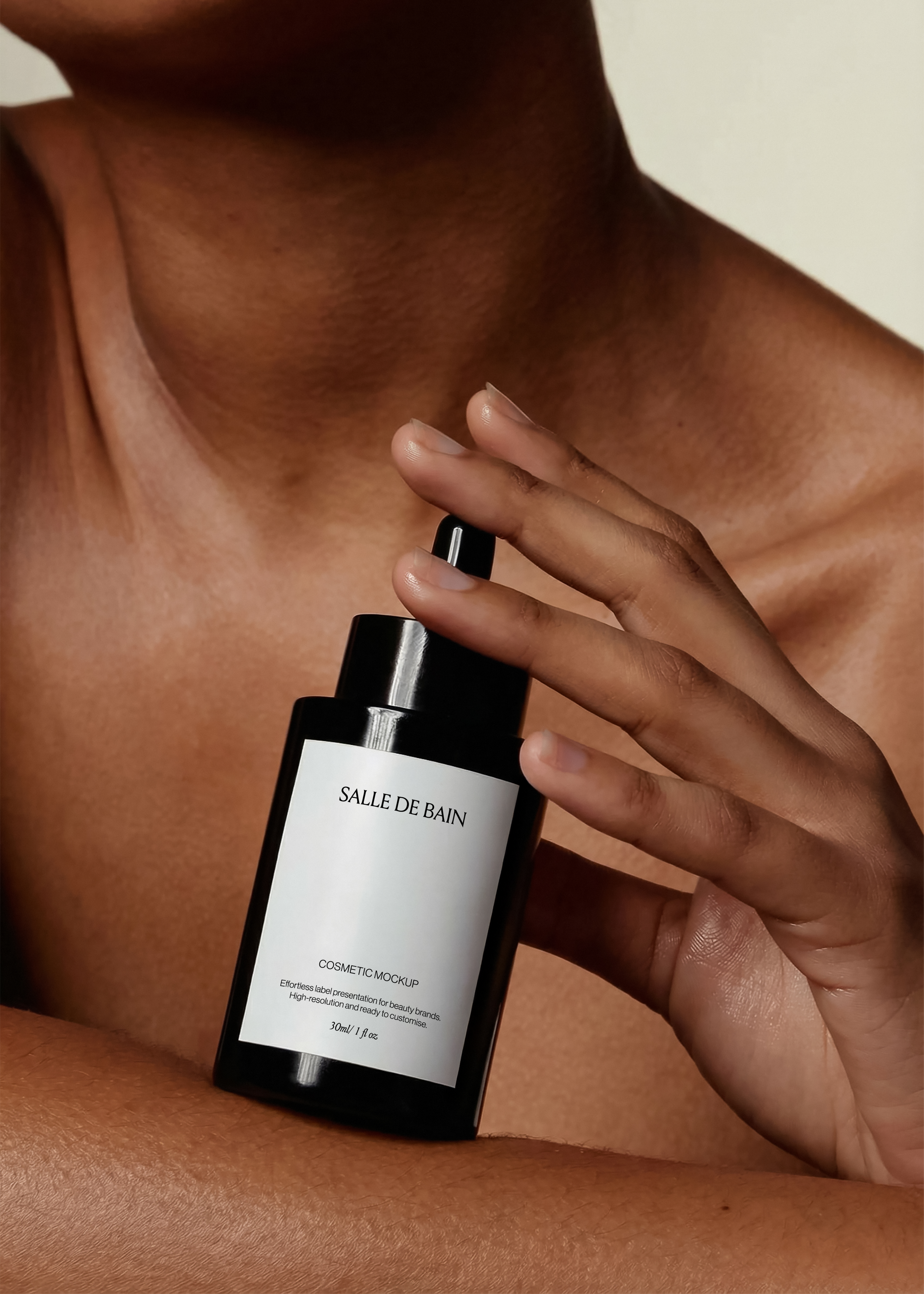 Black dropper bottle mockup with white label held against a collarbone, warm skin and cream backdrop