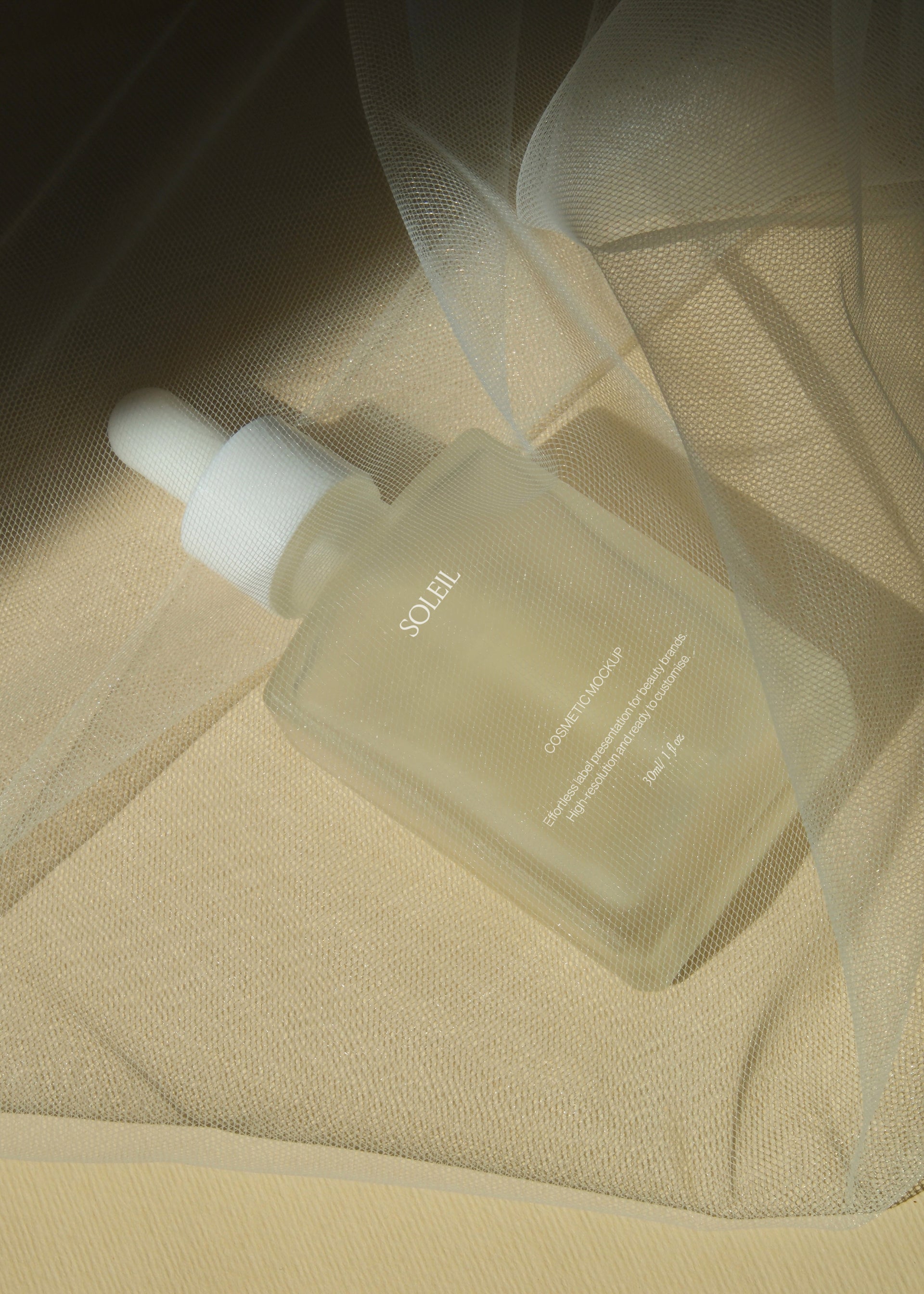 Frosted glass dropper bottle wrapped in sheer golden tulle fabric, diagonal drape with soft warm light and folds