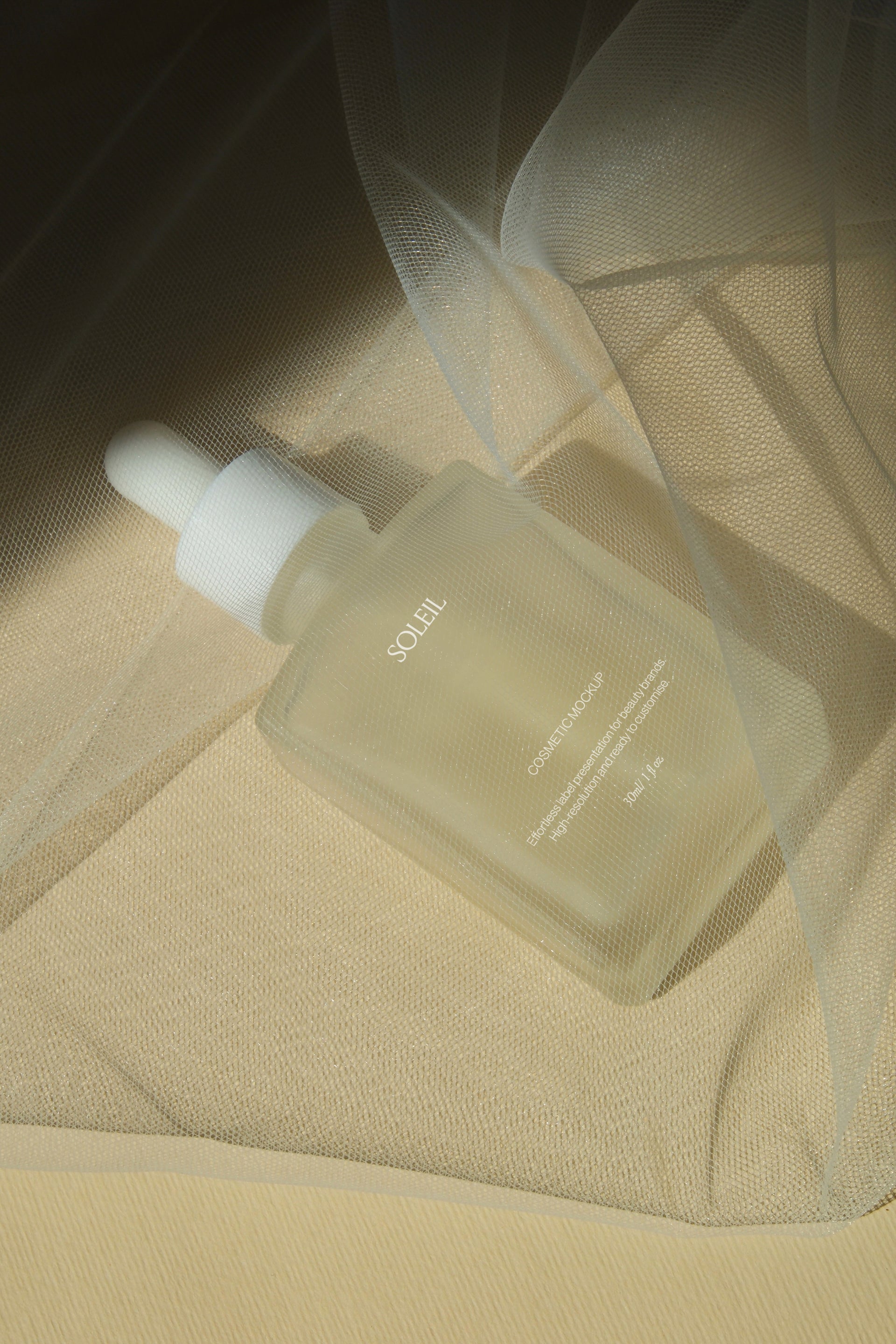 Frosted glass dropper bottle wrapped in sheer golden tulle fabric, diagonal drape with soft warm light and folds