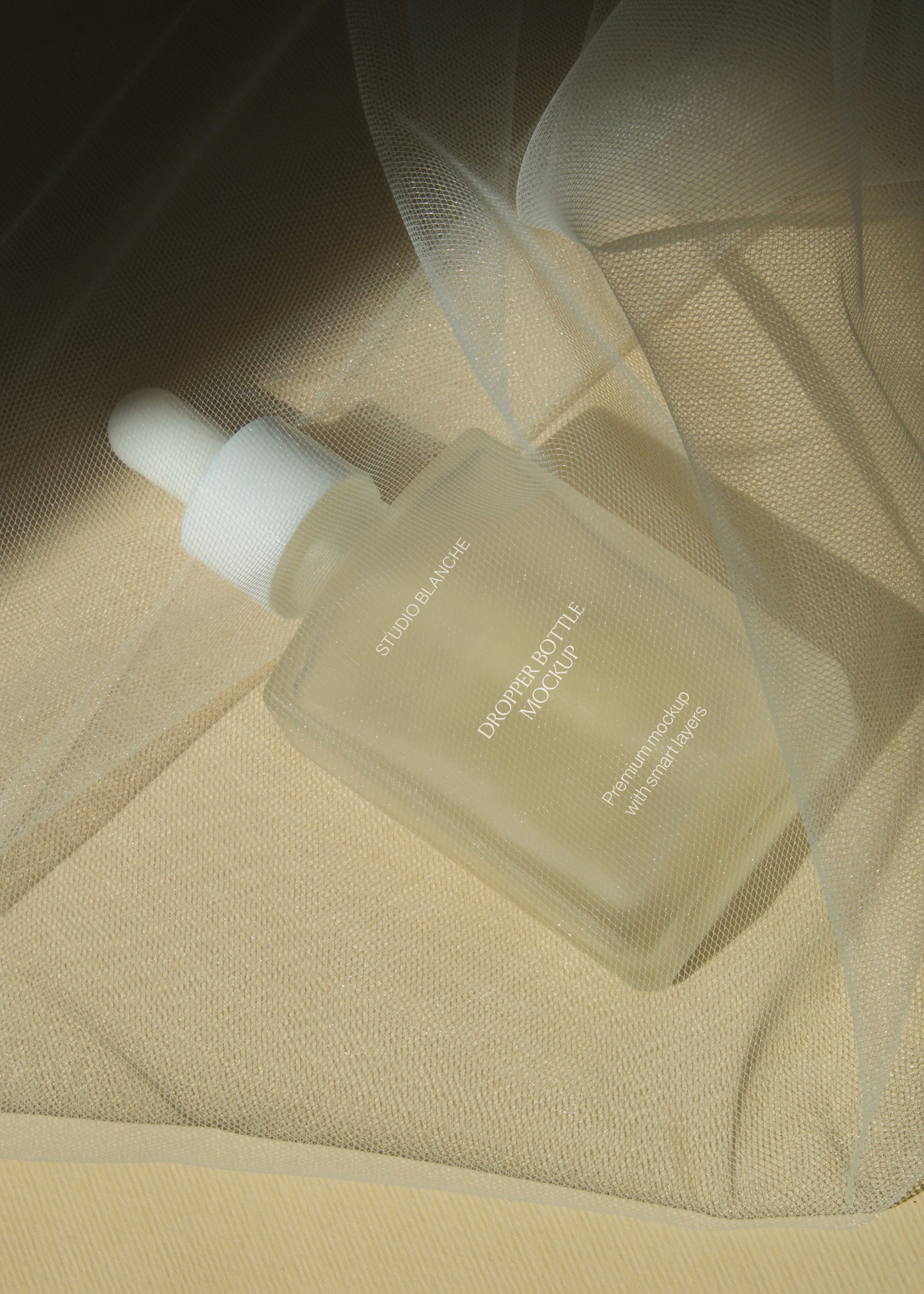 Frosted dropper bottle mockup nestled beneath layered tulle netting, close detail view with warm ambient tone