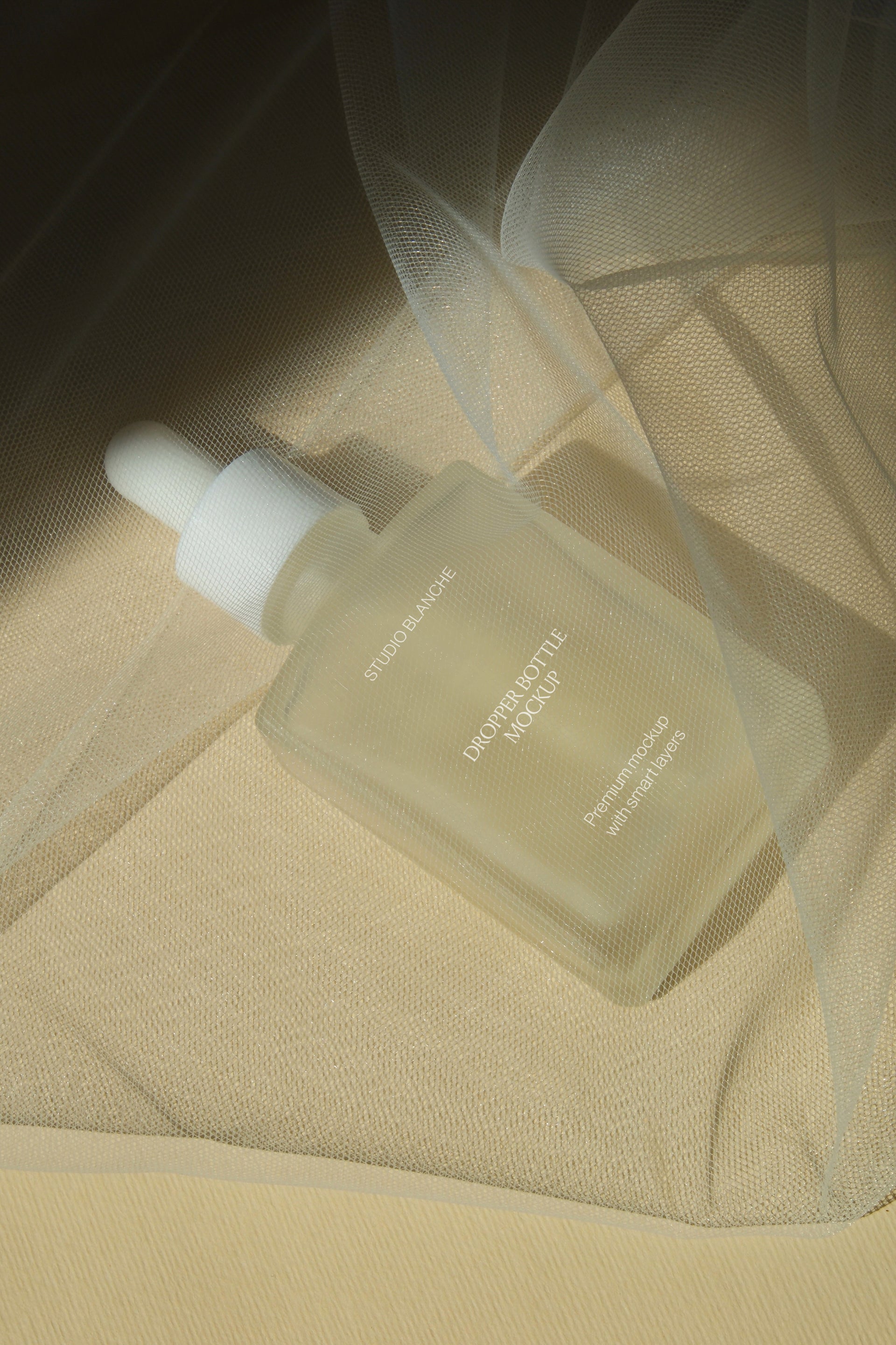 Frosted dropper bottle mockup nestled beneath layered tulle netting, close detail view with warm ambient tone