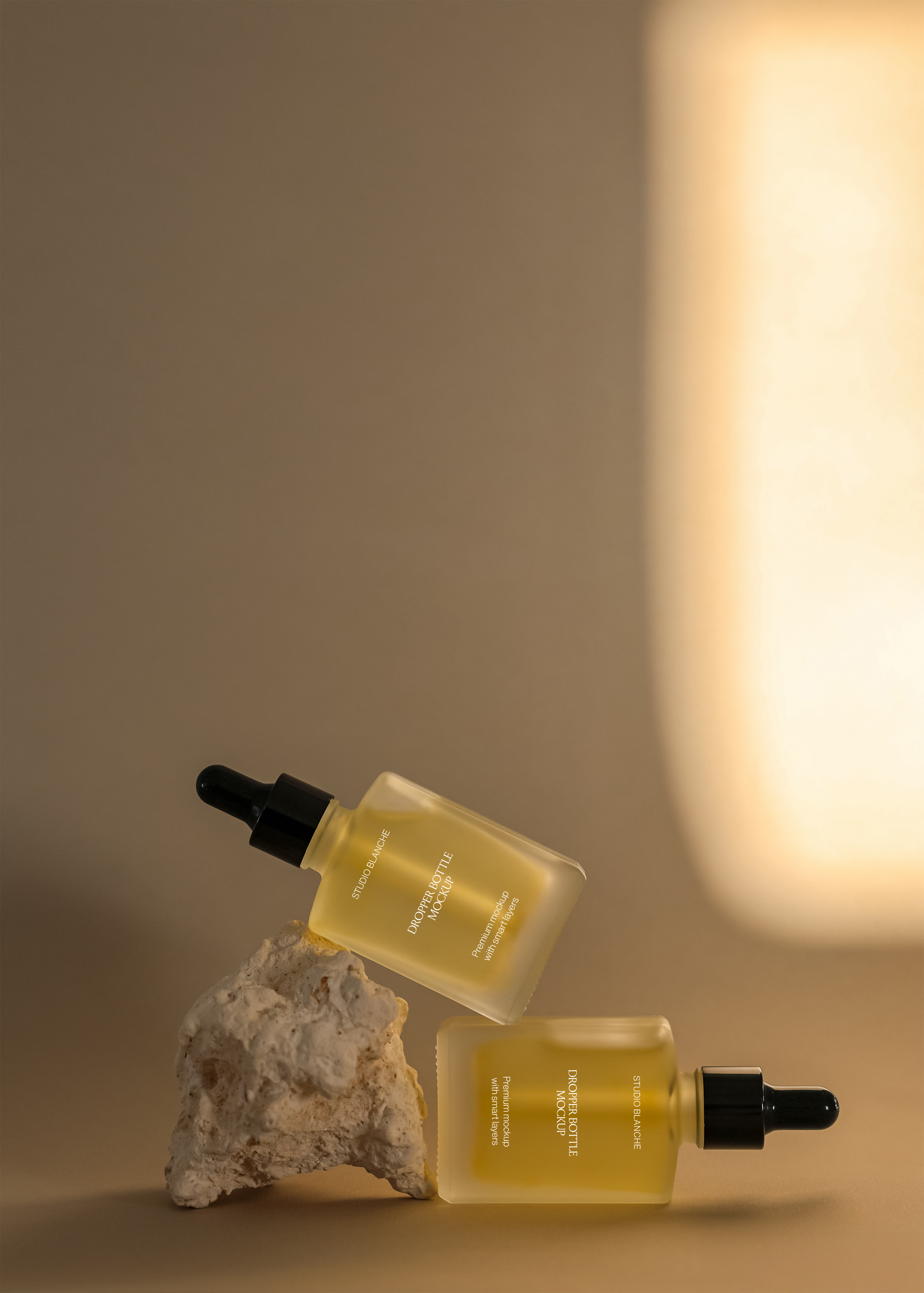 Frosted dropper bottle duo mockup with black pipette caps hovering near stone prop, warm amber tone on tan surface