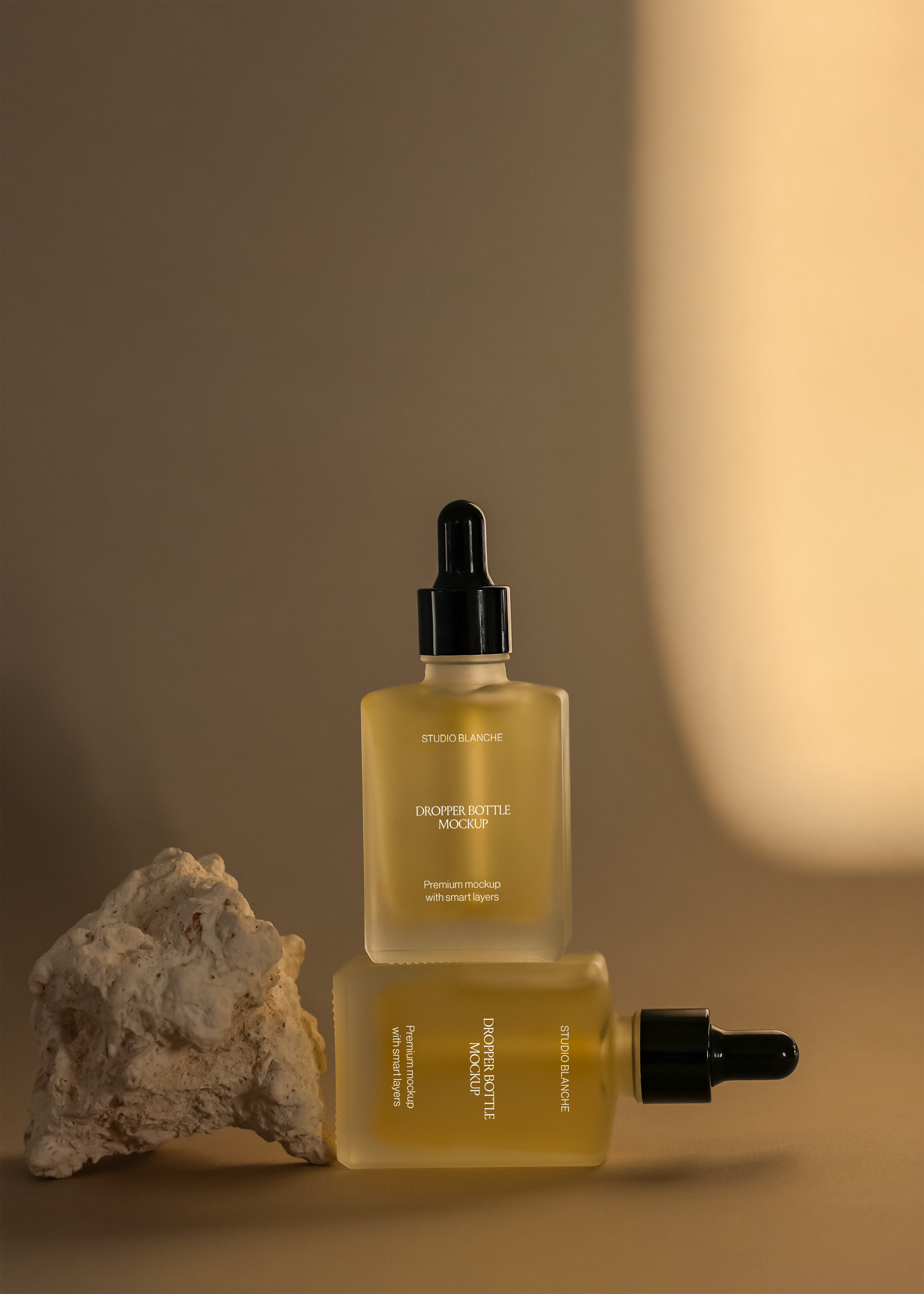 Frosted dropper bottle duo mockup stacked with stone prop, warm amber tone version on tan surface with soft glow