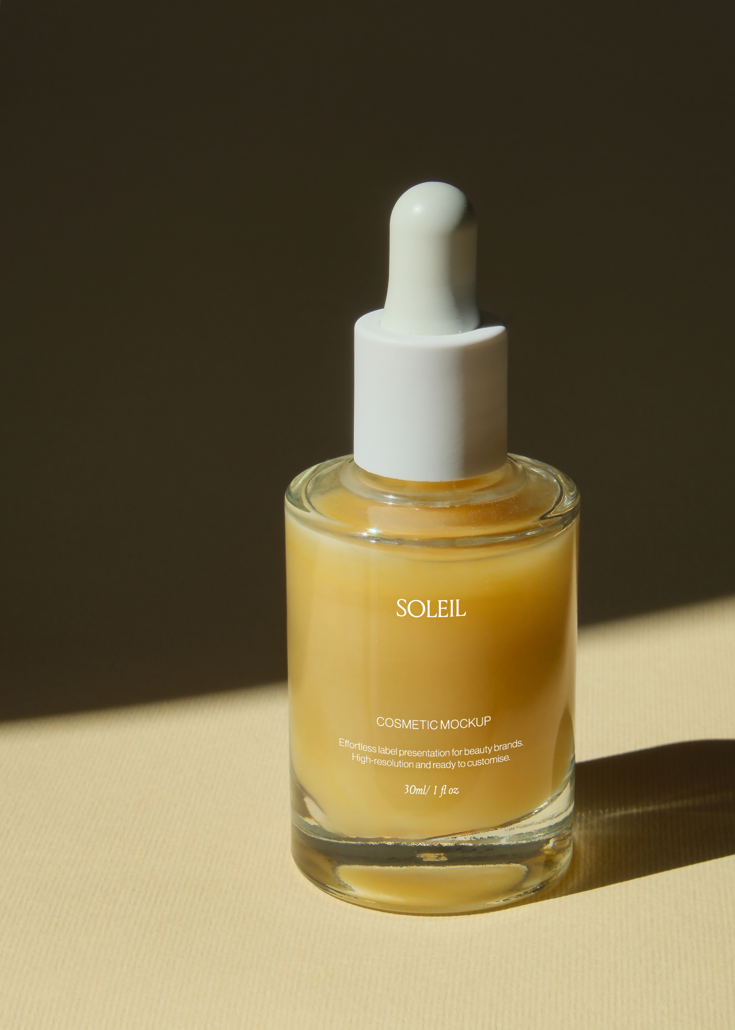 Glass dropper bottle mockup angled on sand-toned surface, amber liquid catching warm side light, dark backdrop