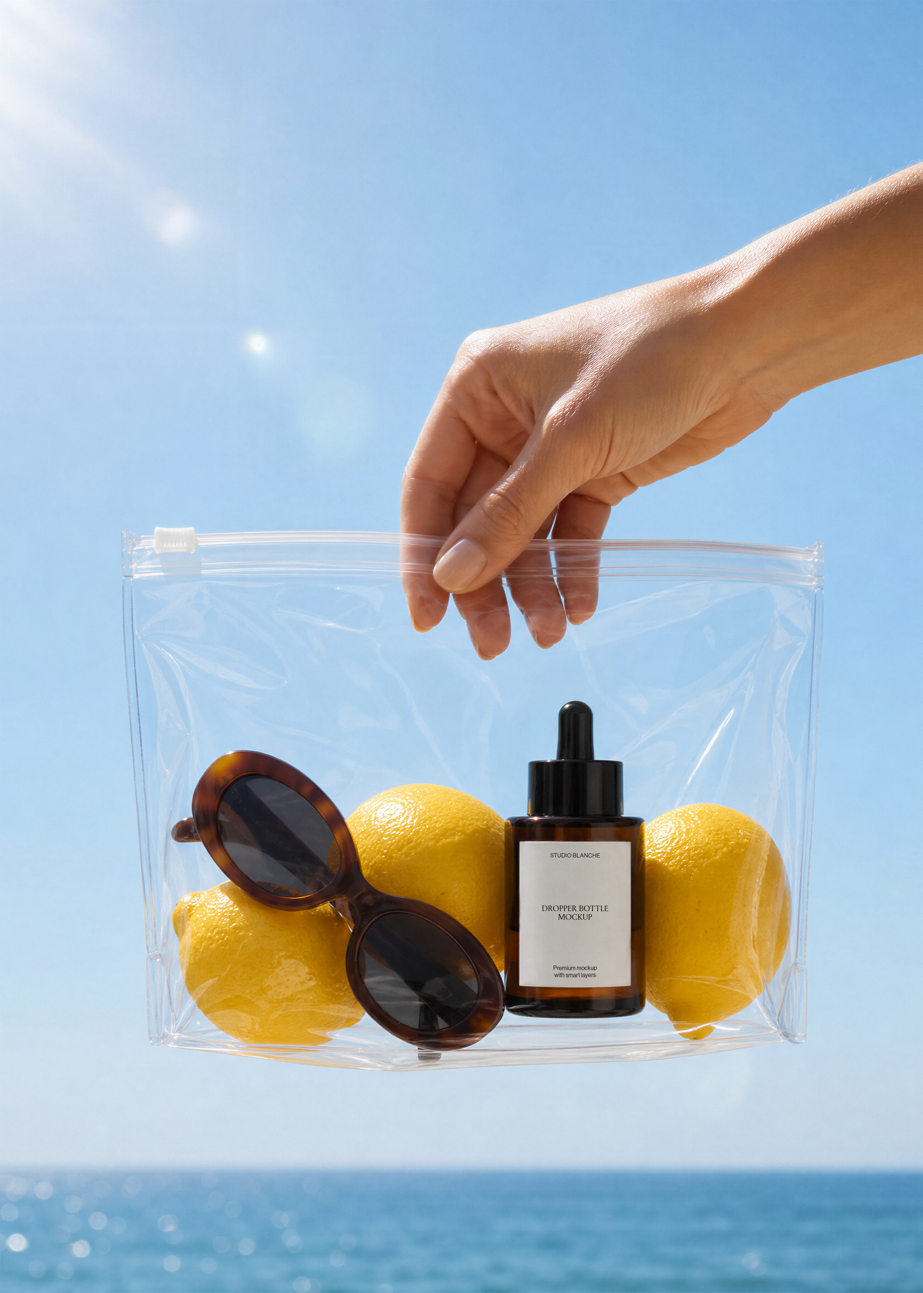 Close view of an amber dropper bottle label in a transparent bag beside lemons and sunglasses, coastal sky and sea