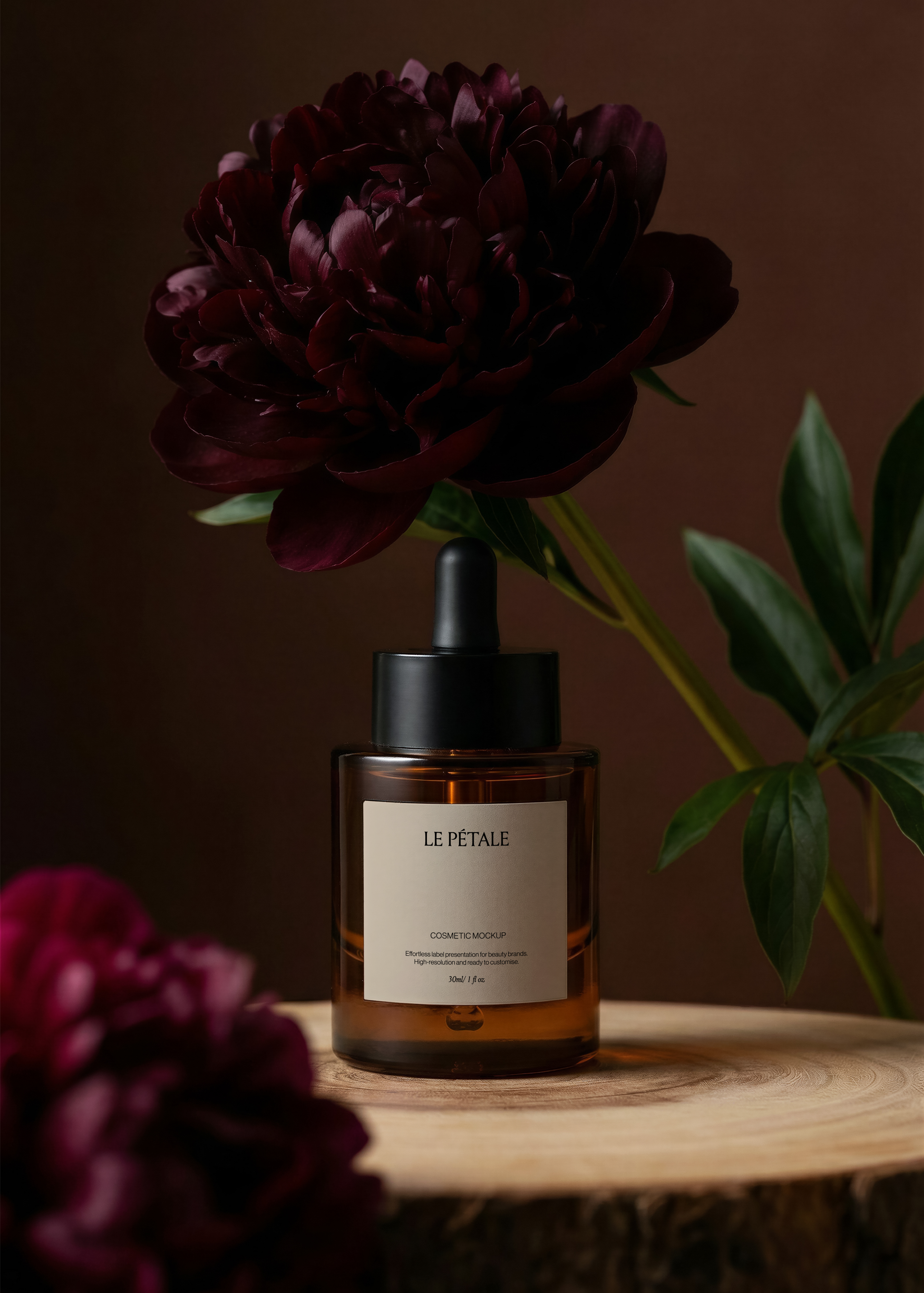 Amber dropper bottle mockup with label, raw wood slice base, burgundy peony overhead, green foliage, dark espresso background