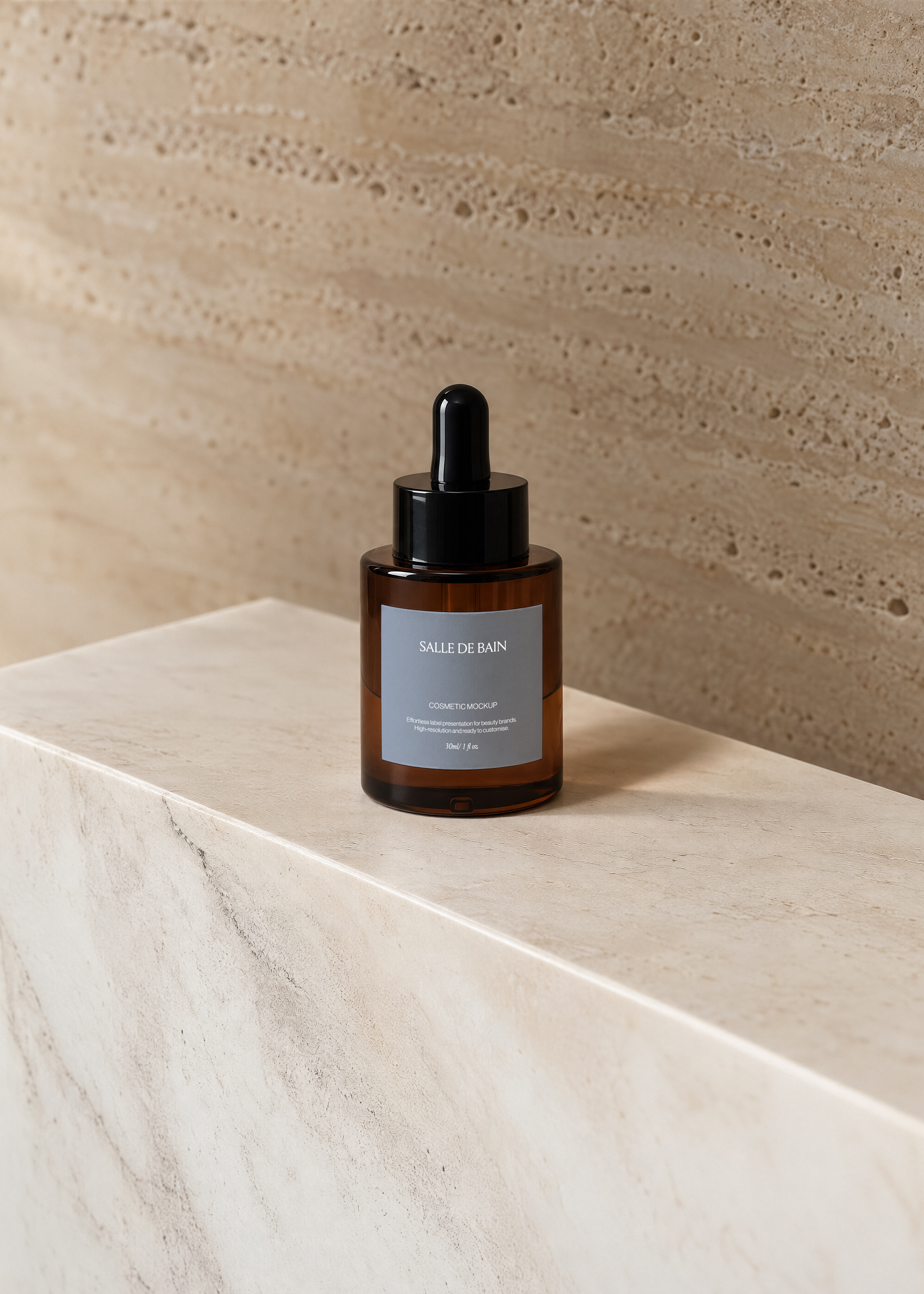 Dropper bottle mockup with dusty blue label on amber glass, black pipette cap, on a beige travertine block in soft light
