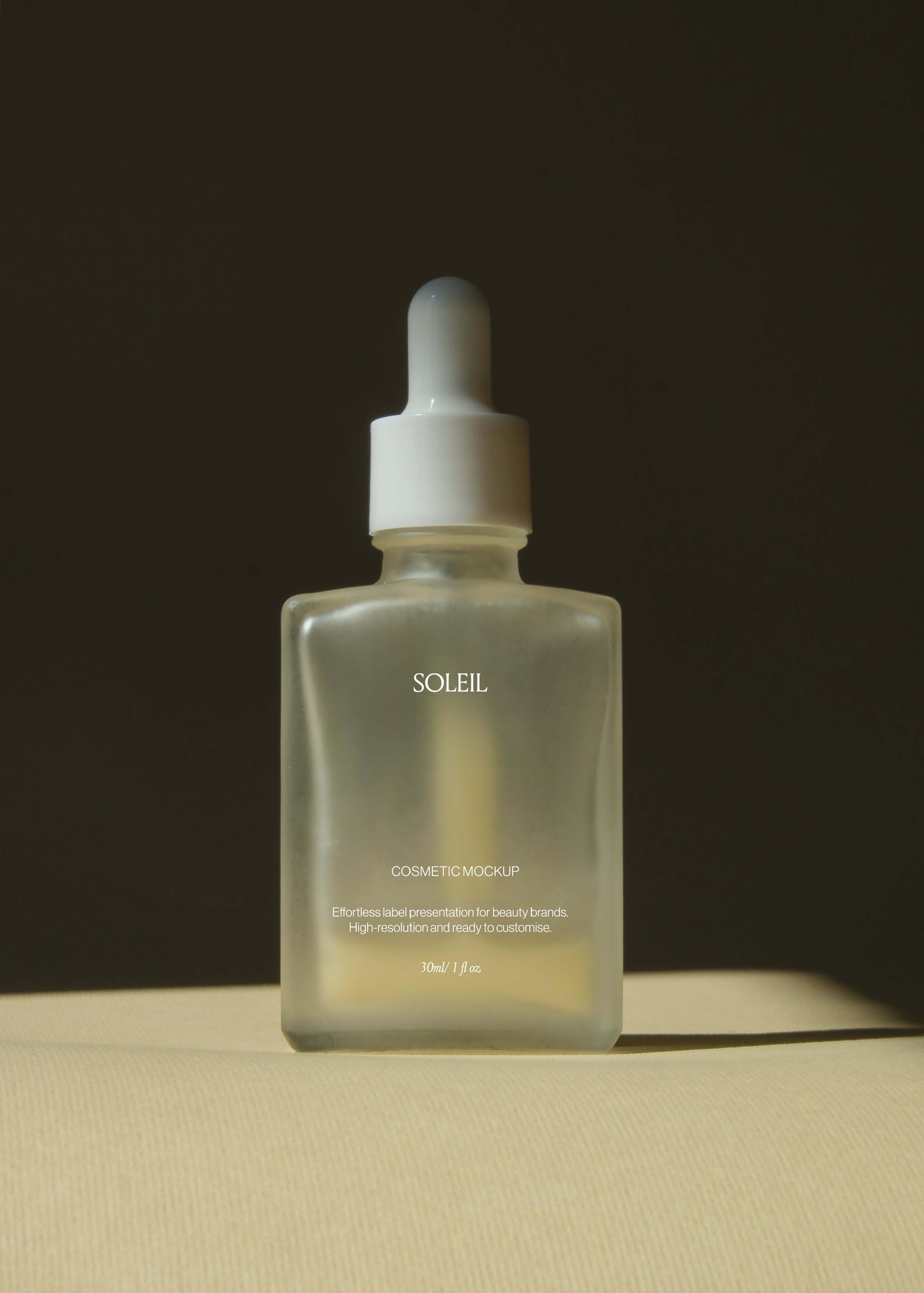 Frosted glass dropper bottle mockup centred against dark backdrop, single light beam down the glass, sand surface