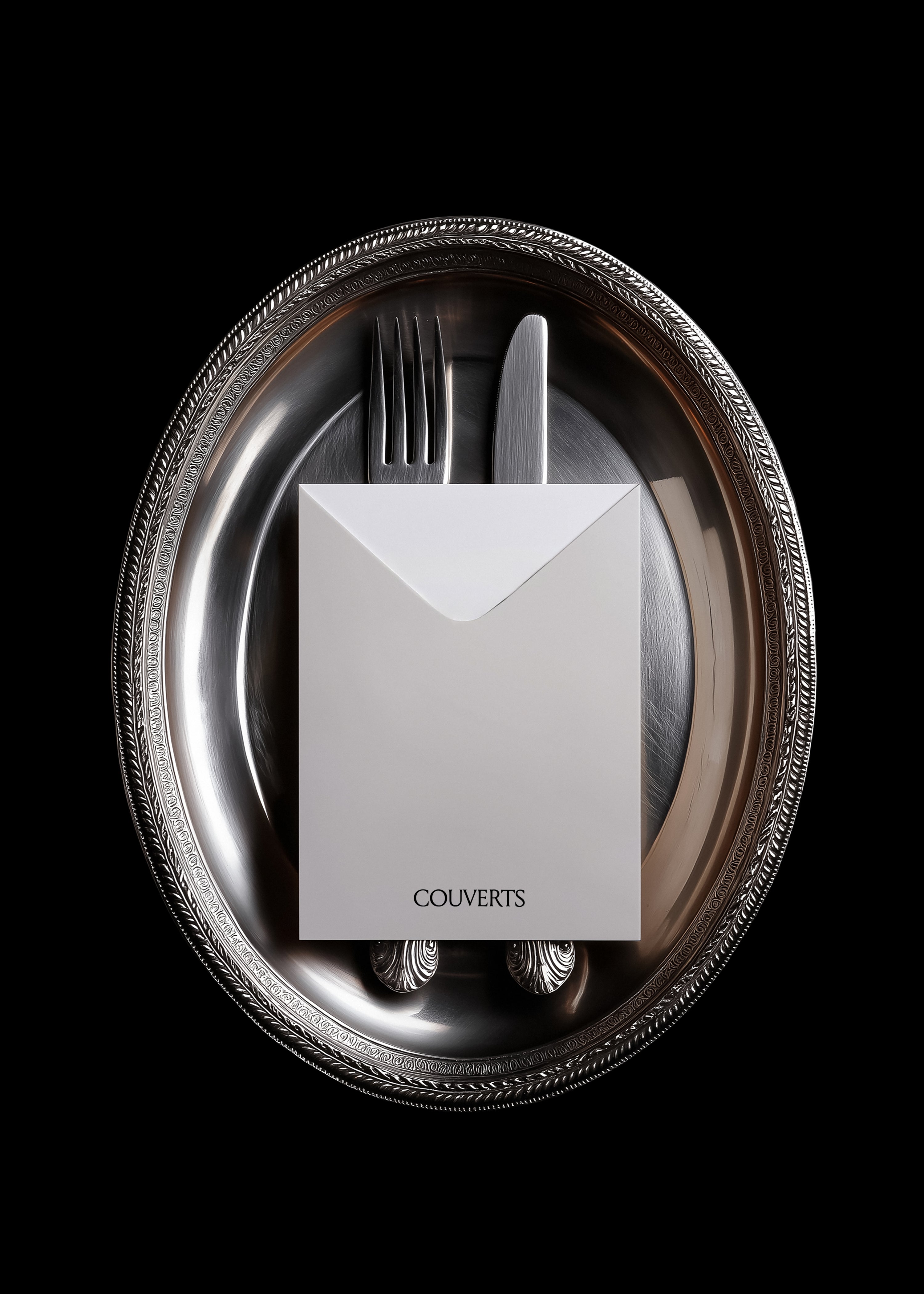White envelope mockup with fork and knife resting on tarnished silver tray, vintage editorial styling, dark background