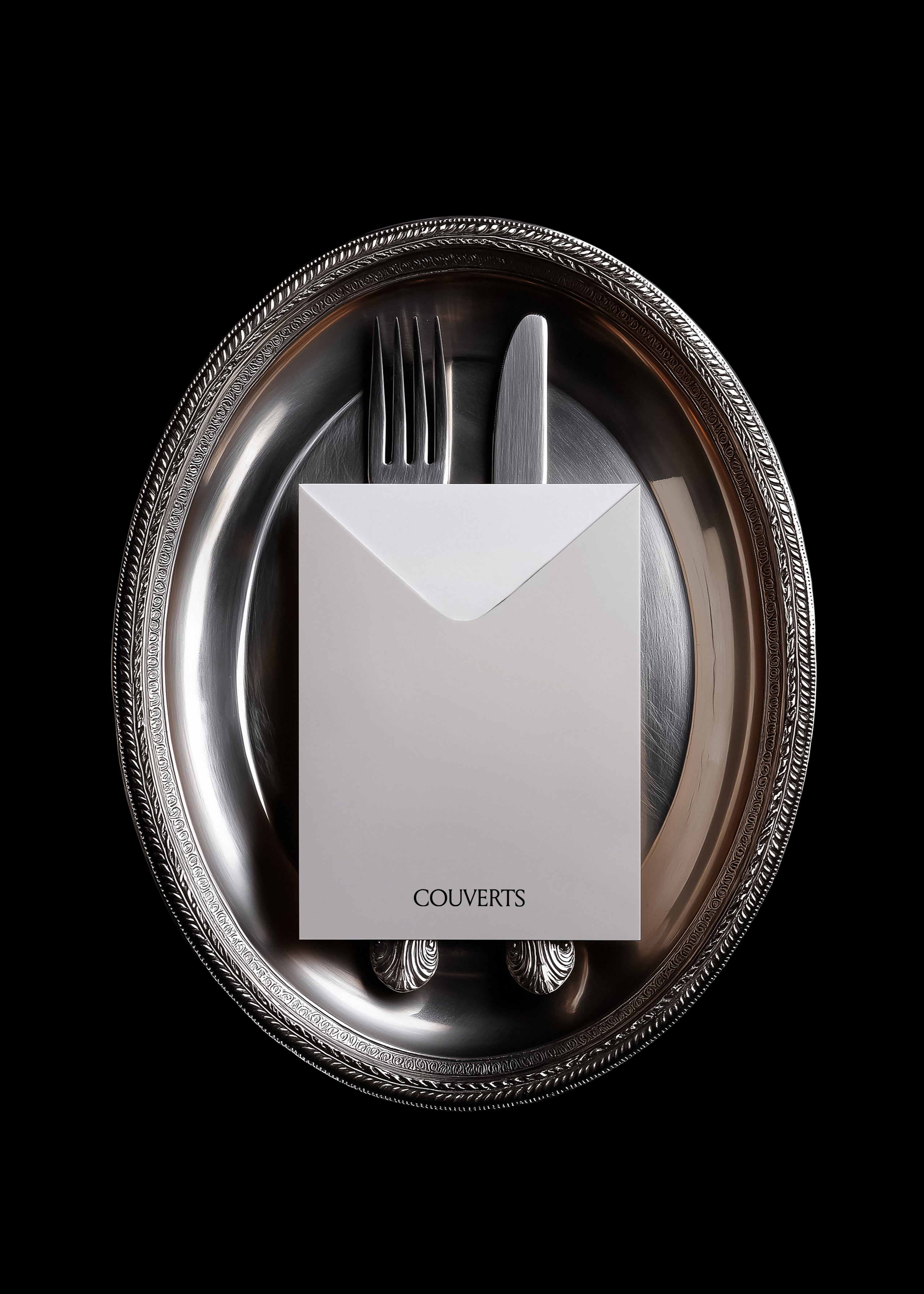 White envelope mockup with fork and knife resting on tarnished silver tray, vintage editorial styling, dark background