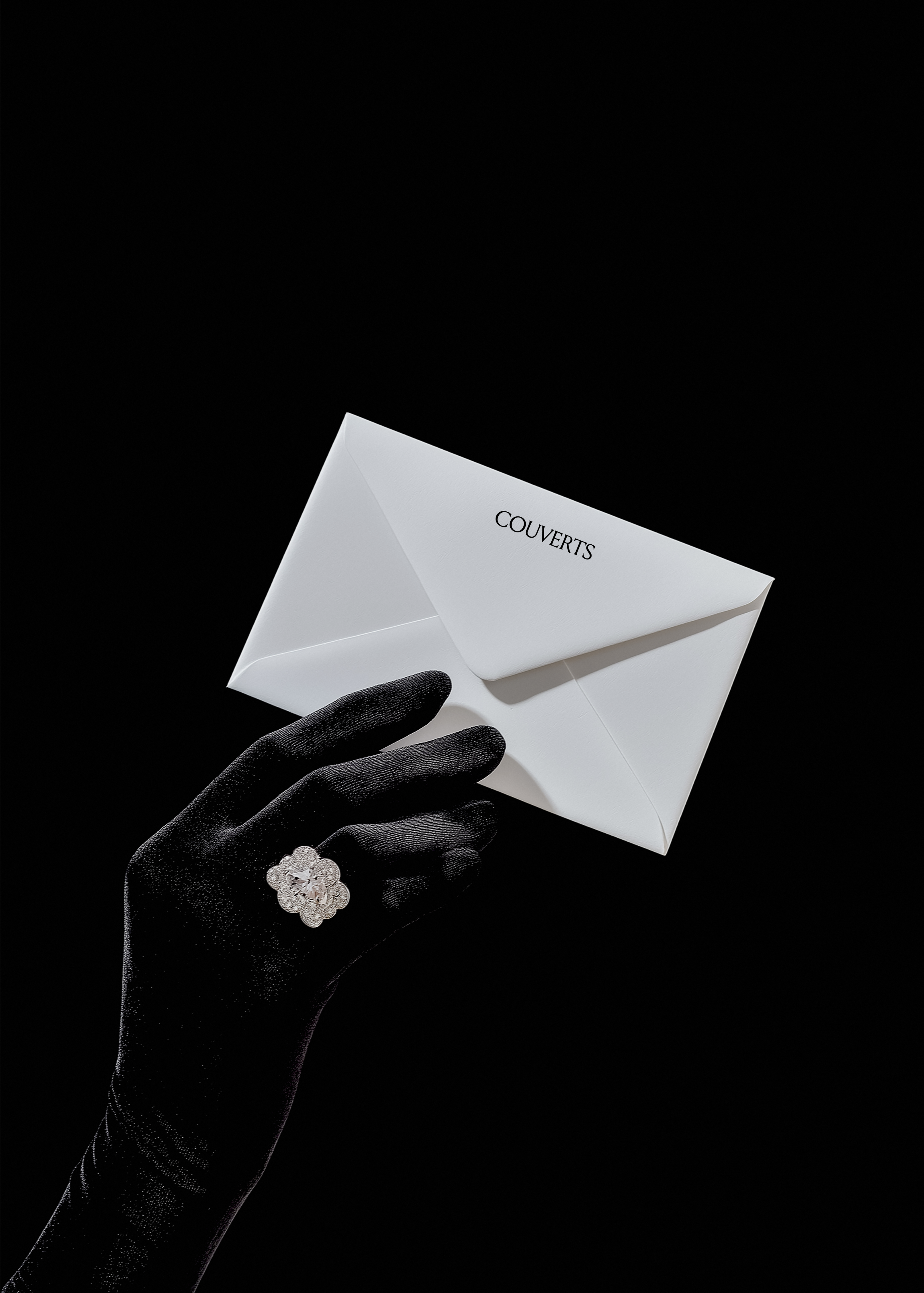 White envelope mockup pinched by black satin gloved hand wearing diamond ring, angled against black background