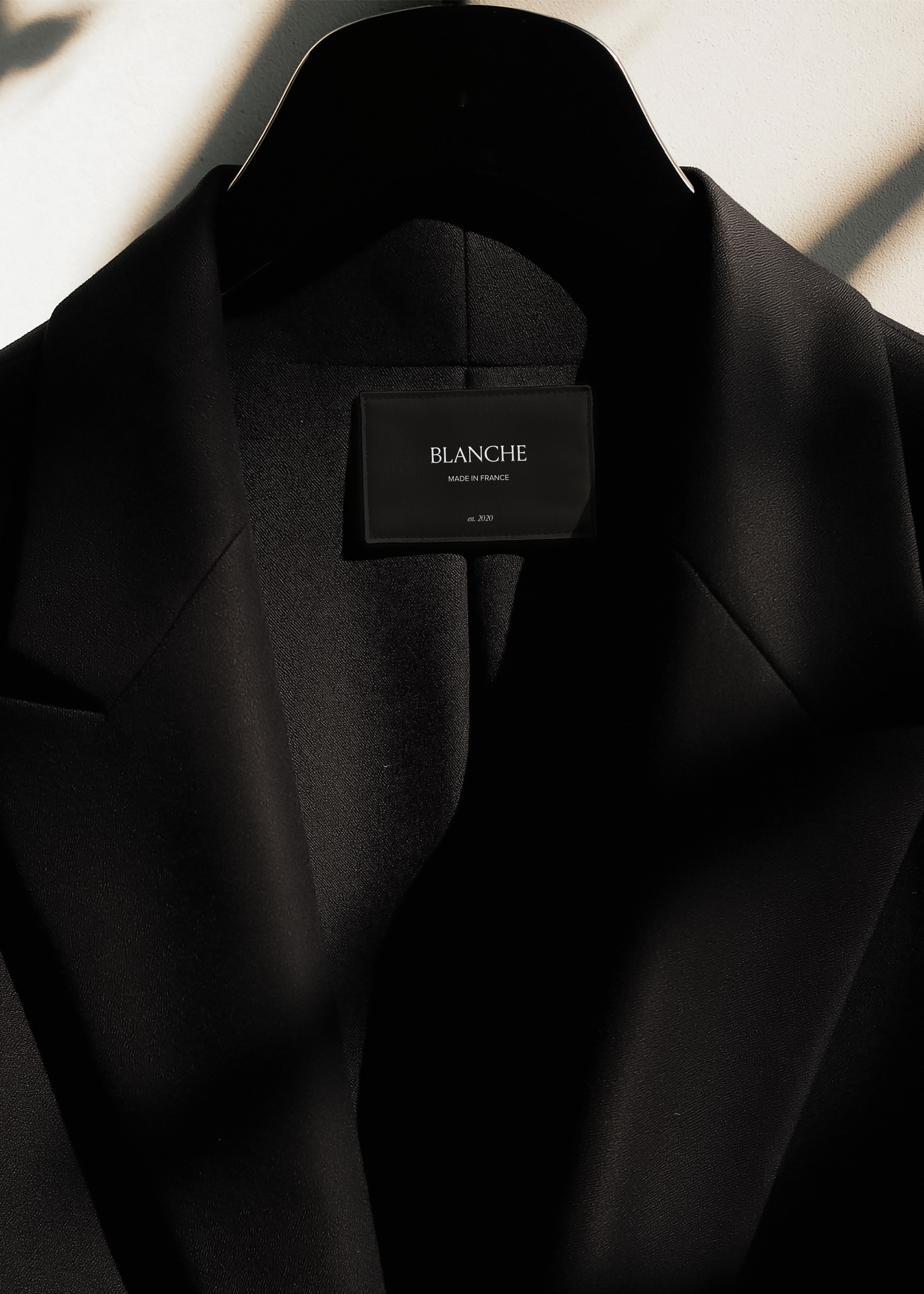 Black garment label on black blazer collar showing white brand name and origin text in serif type, editorial lighting