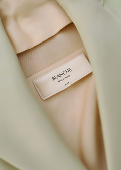 Close-up woven garment label on sage blazer satin lining showing brand name and origin text in serif and sans-serif type