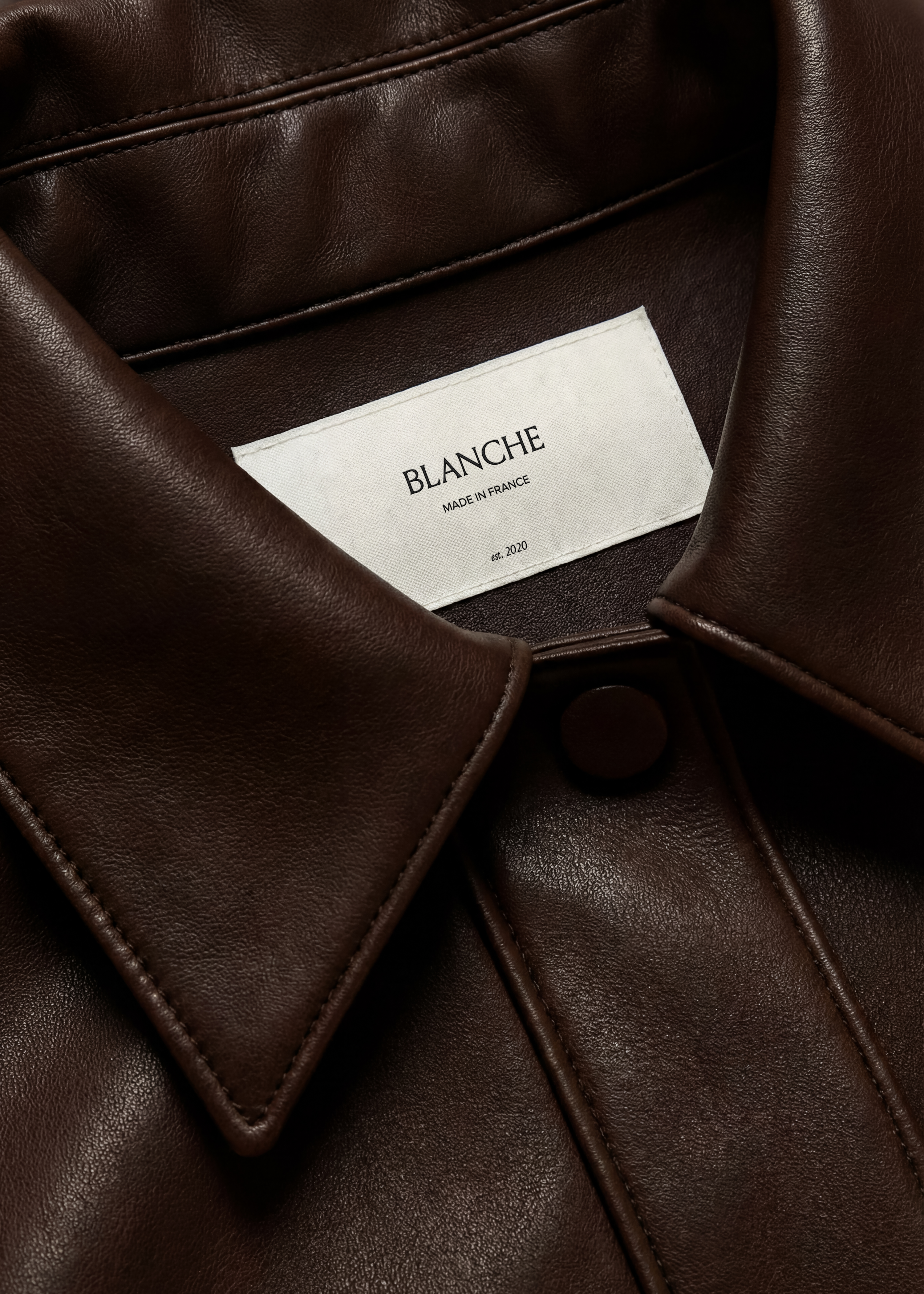 Linen garment label mockup stitched inside the collar of a chocolate leather jacket, soft pebbled grain close-up