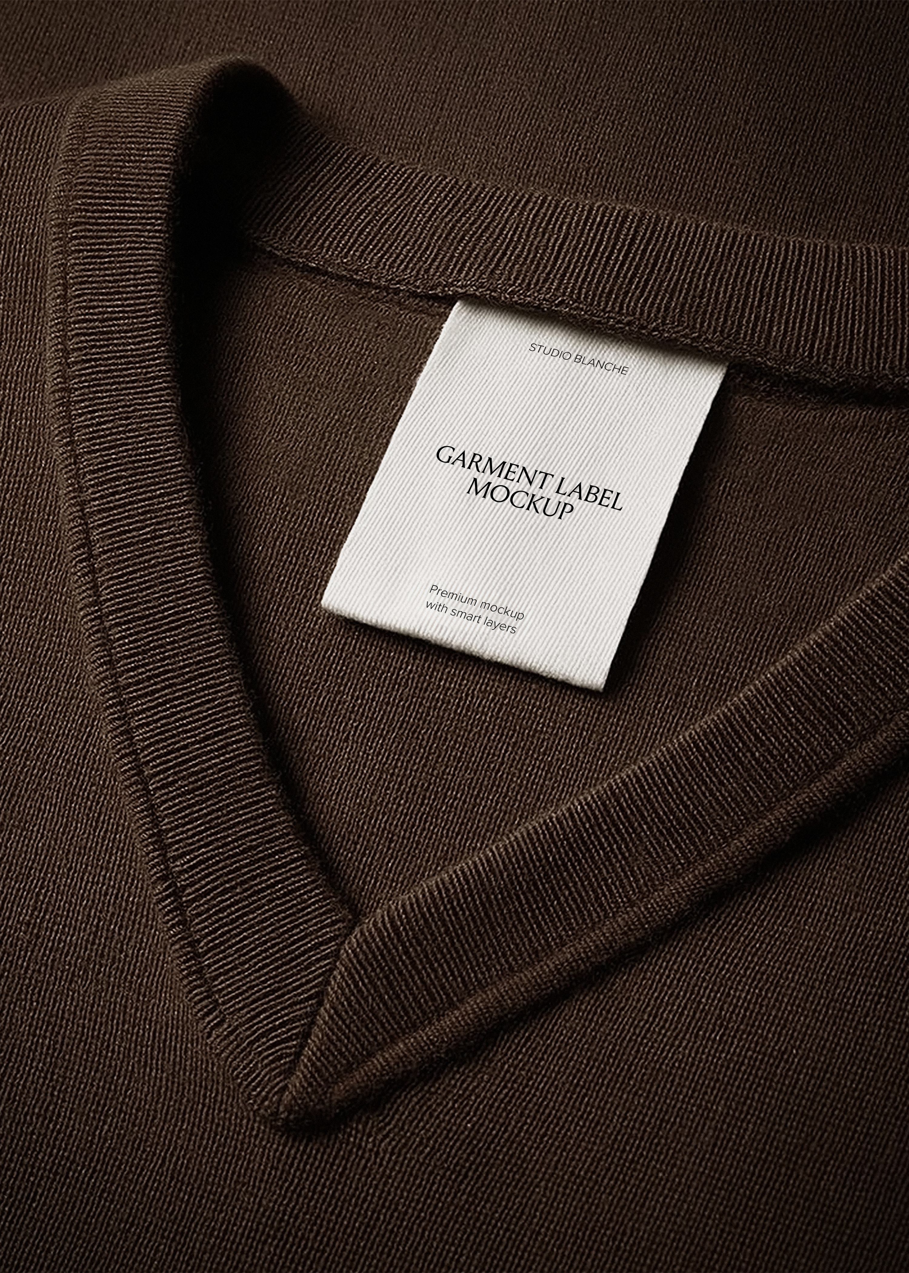 White woven garment label mockup inside v-neckline of deep chocolate brown knit jumper, close-up editorial styling