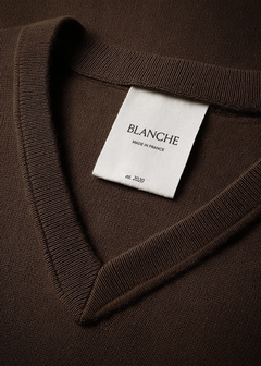 Close-up woven garment label on brown v-neck knit showing brand name and origin text in serif type