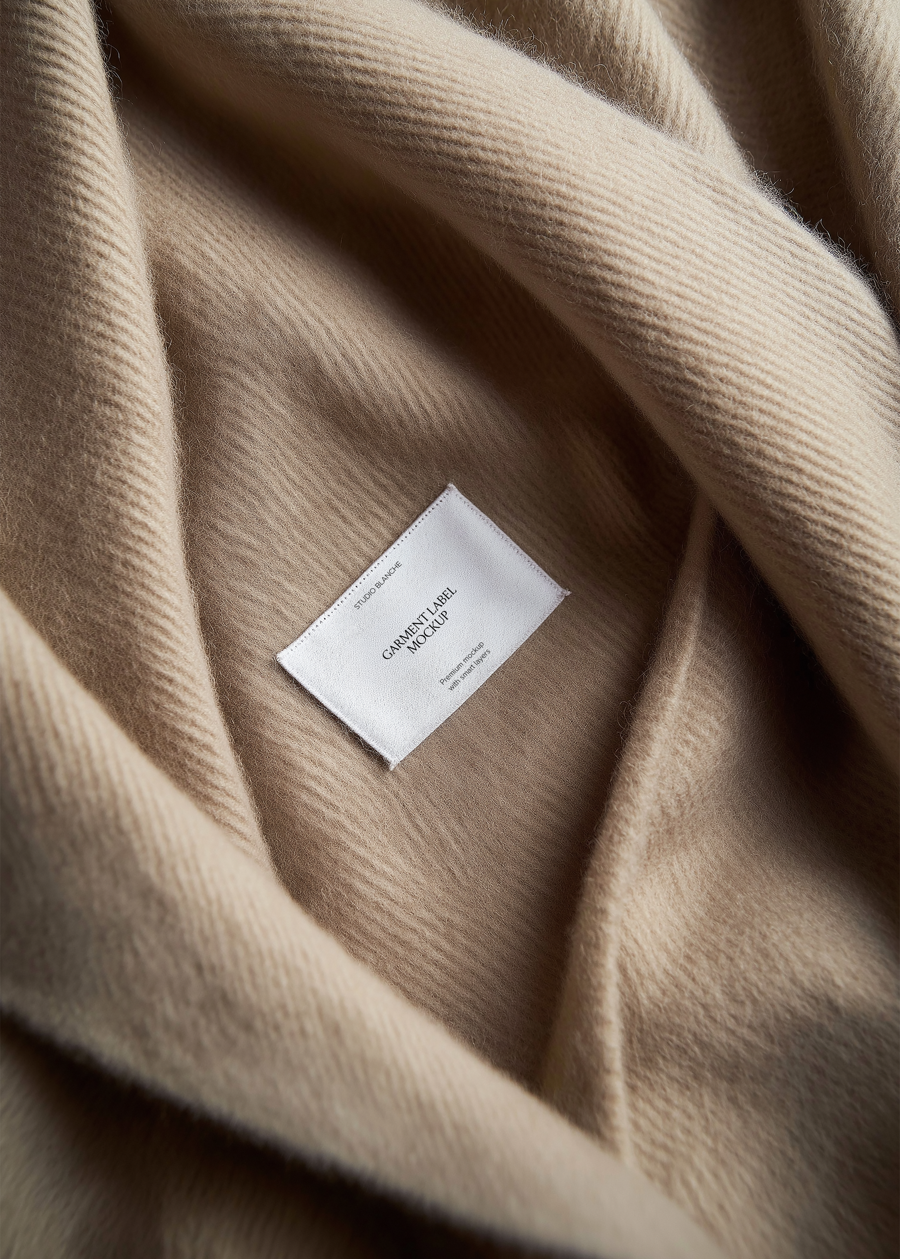 White woven garment label mockup nestled within draped folds of taupe cashmere knit, close-up editorial styling