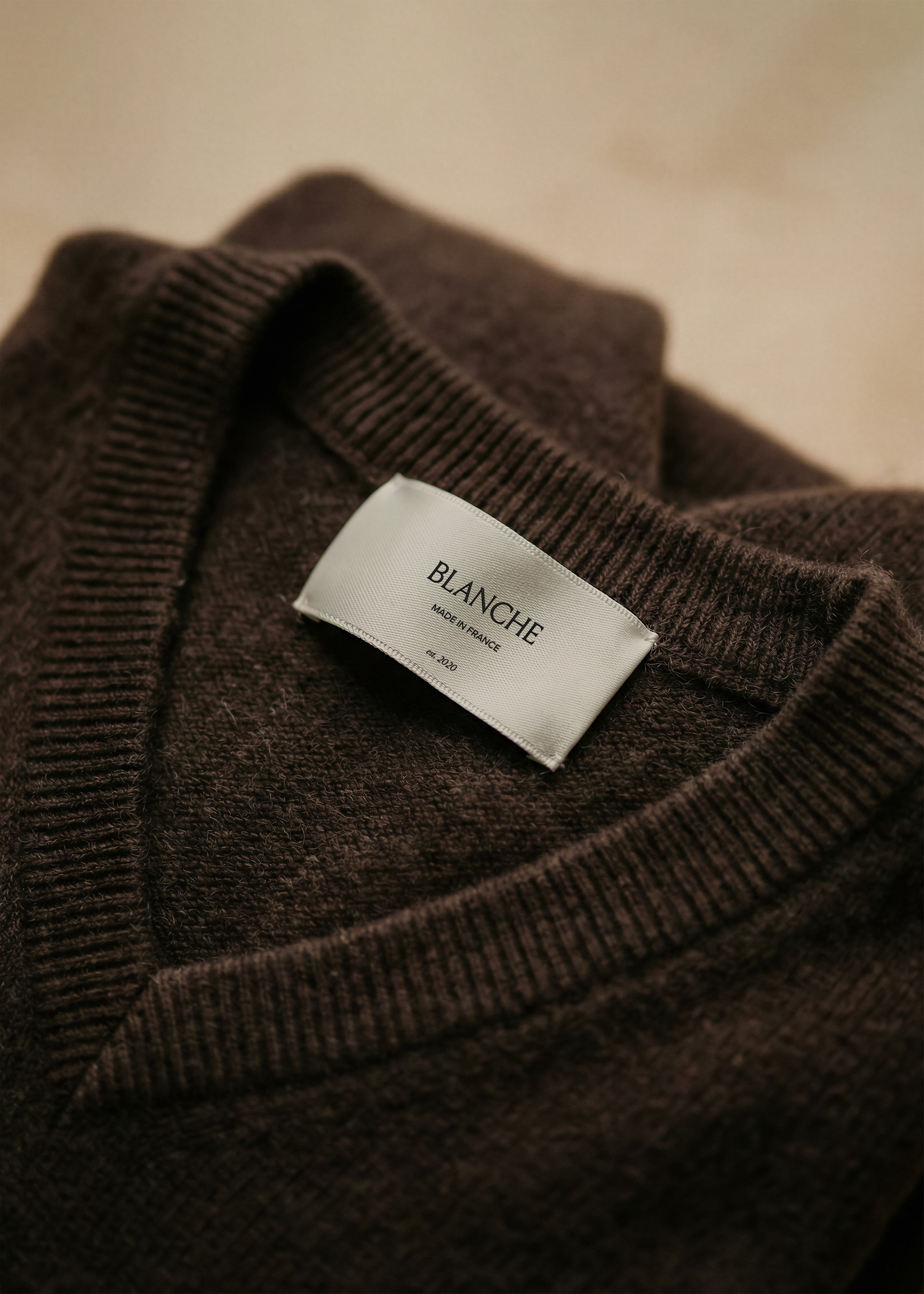 Garment label mockup stitched into the neckline of a folded chocolate cashmere v-neck jumper, soft natural lighting