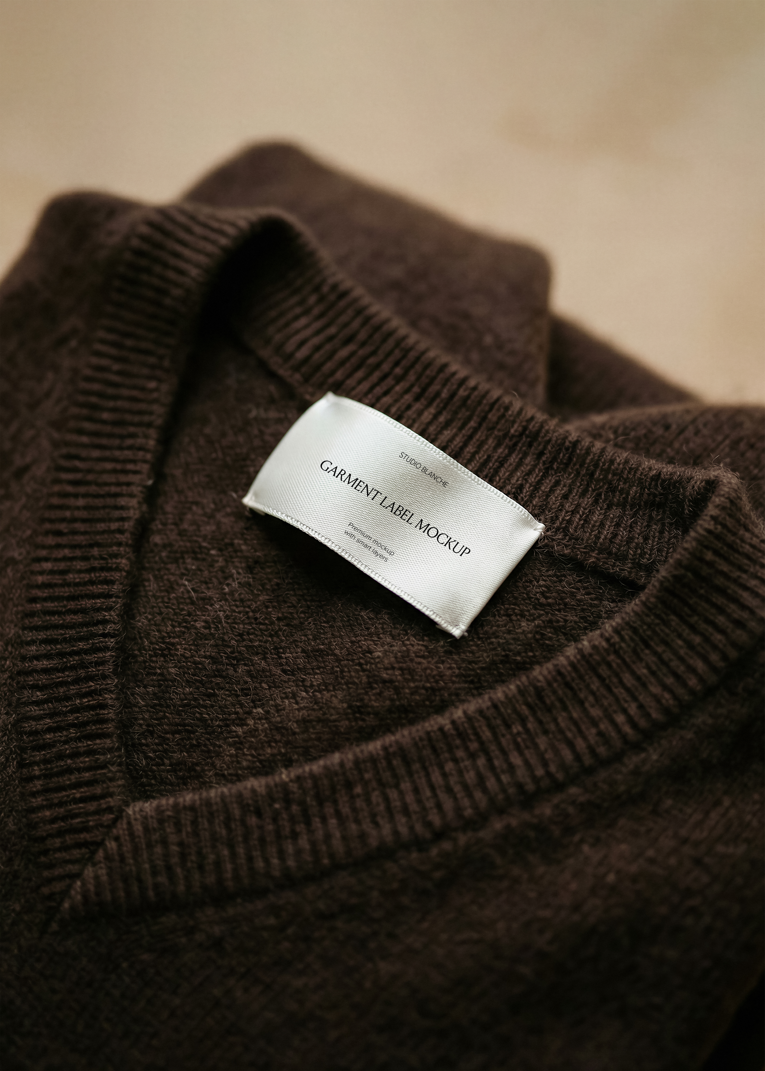 Satin garment label mockup on ribbed knit neckline of a brown wool jumper, close-up tactile fashion brand styling