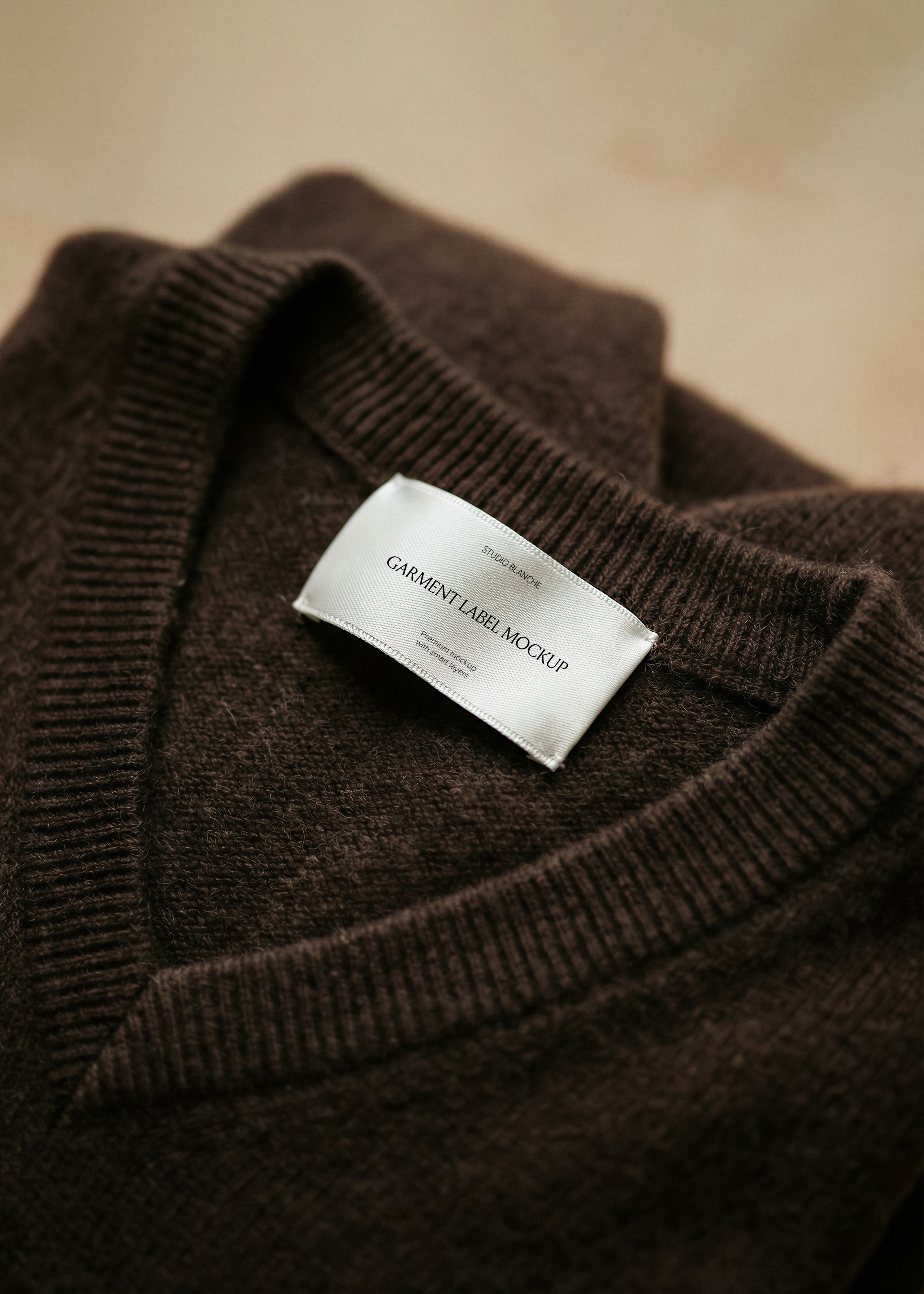 Satin garment label mockup on ribbed knit neckline of a brown wool jumper, close-up tactile fashion brand styling