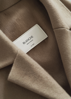 Close-up garment label on taupe coat interior showing brand name and origin text in serif and sans-serif type