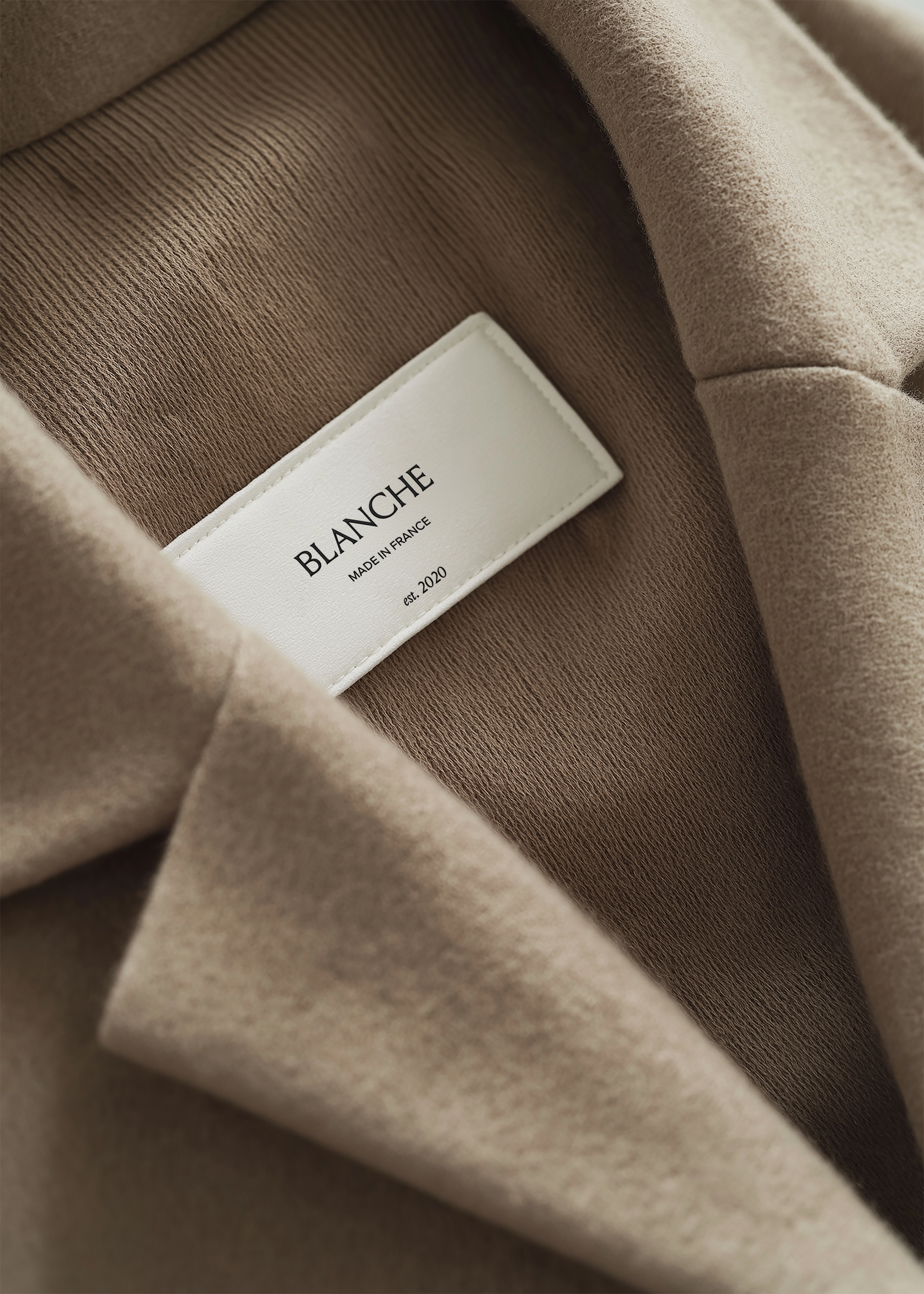 Close-up garment label on taupe coat interior showing brand name and origin text in serif and sans-serif type