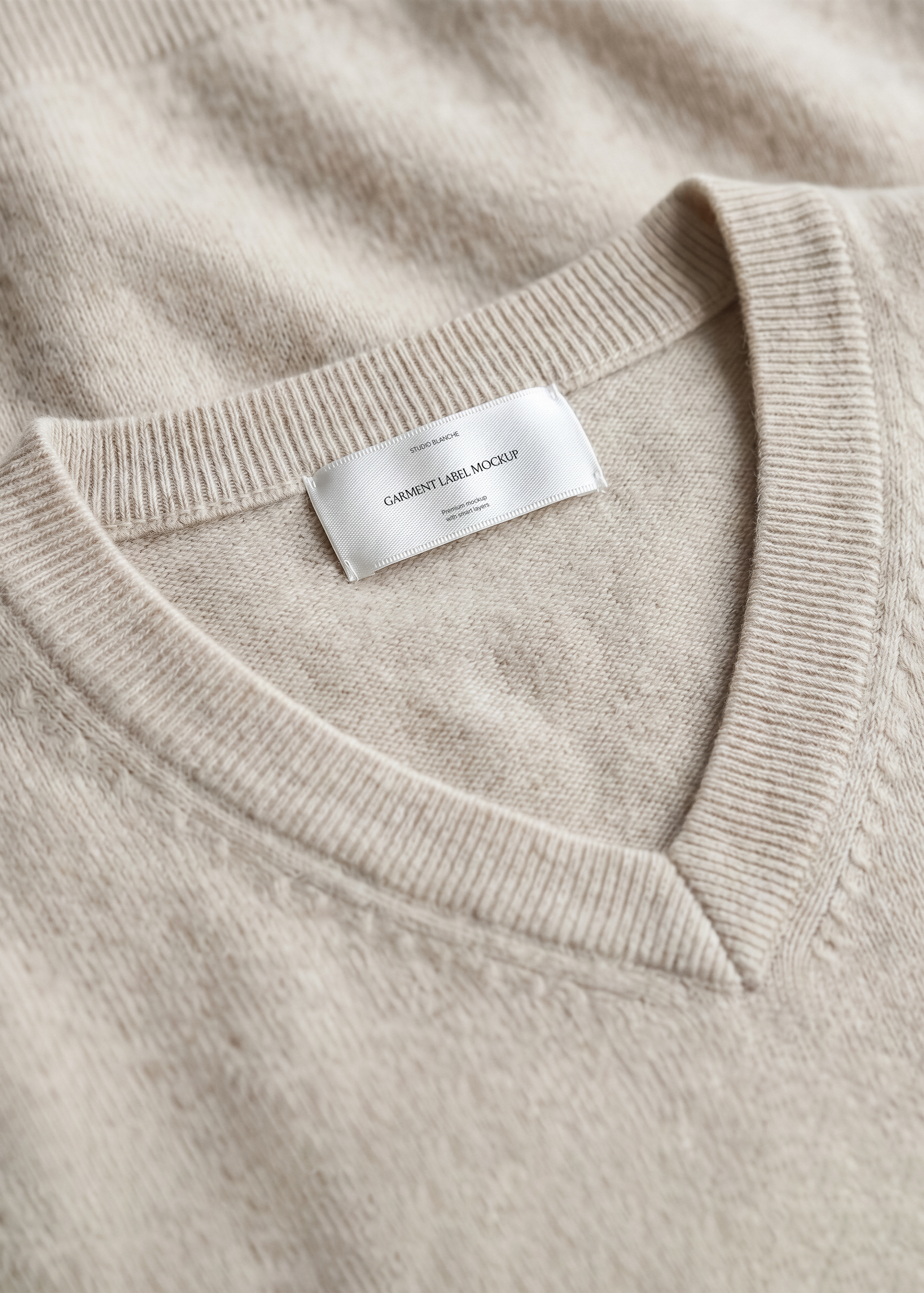 Woven garment label mockup on flecked beige knit collar, ribbed v-neckline detail, neutral slow fashion styling
