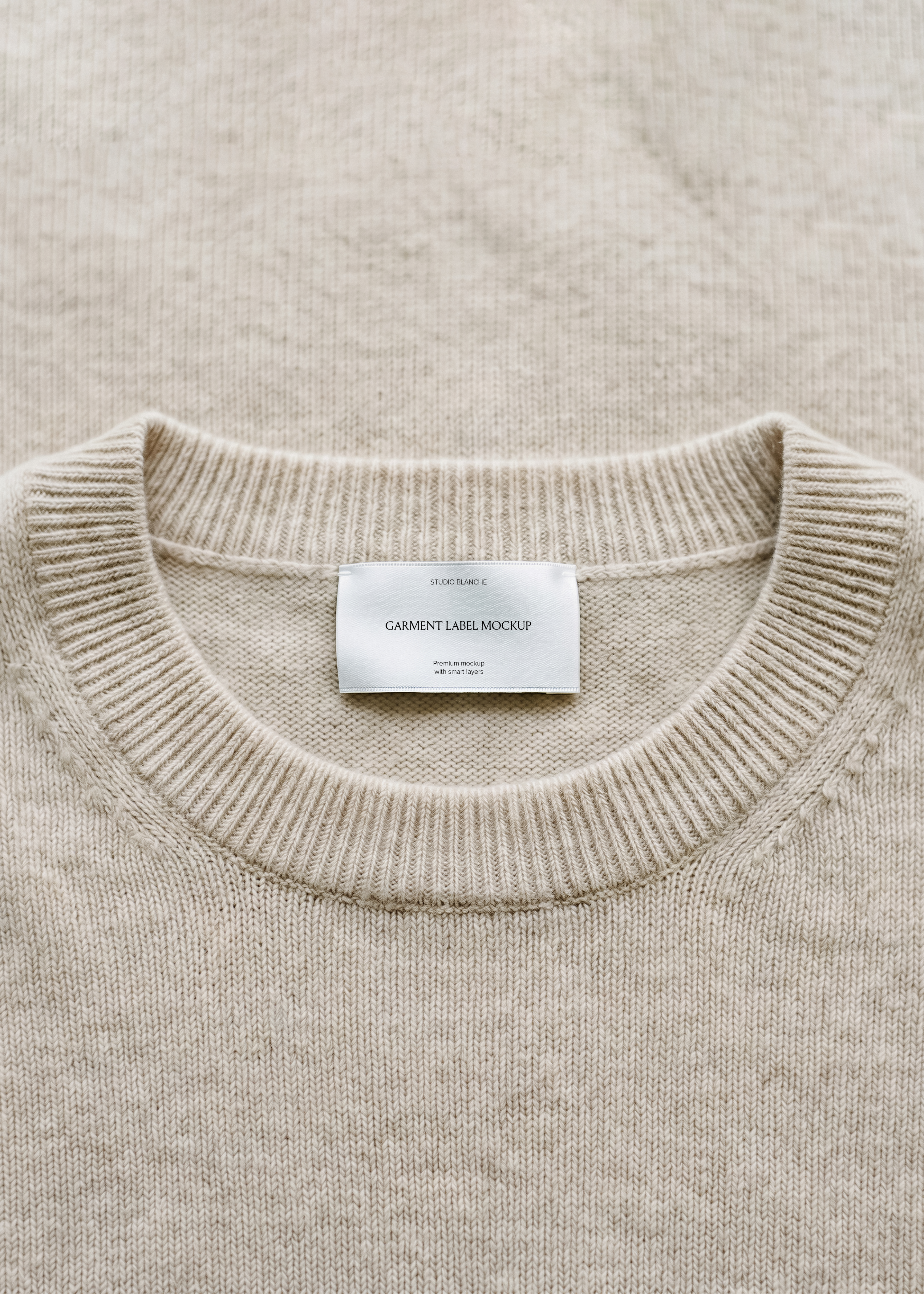 Woven garment label mockup on flecked beige knit collar, ribbed crew neckline, neutral slow fashion close-up