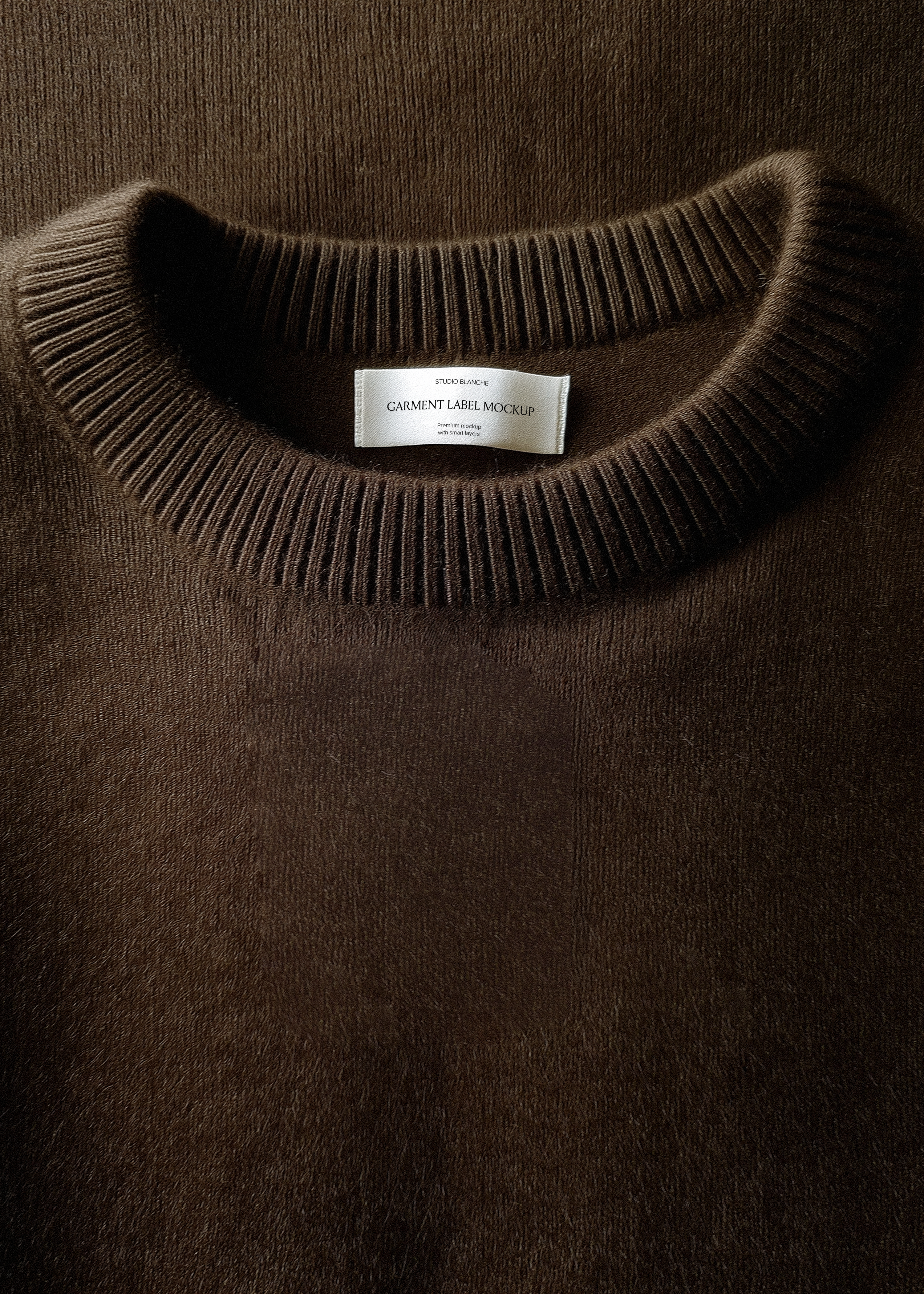 White satin garment label mockup inside ribbed neckline of deep brown knit jumper, close-up editorial styling