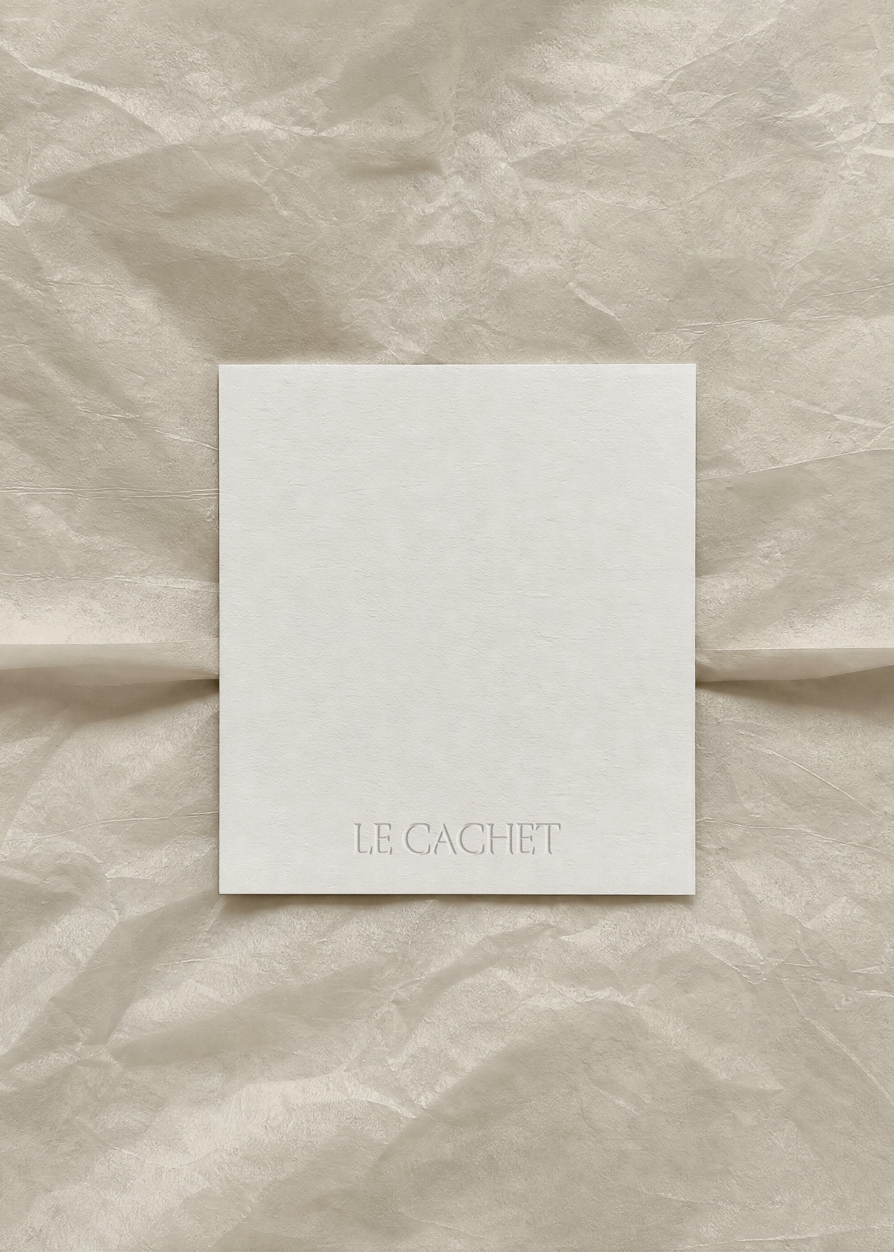 Blank white label card on crumpled beige tissue paper, embossed logo detail, tonal minimal flat lay