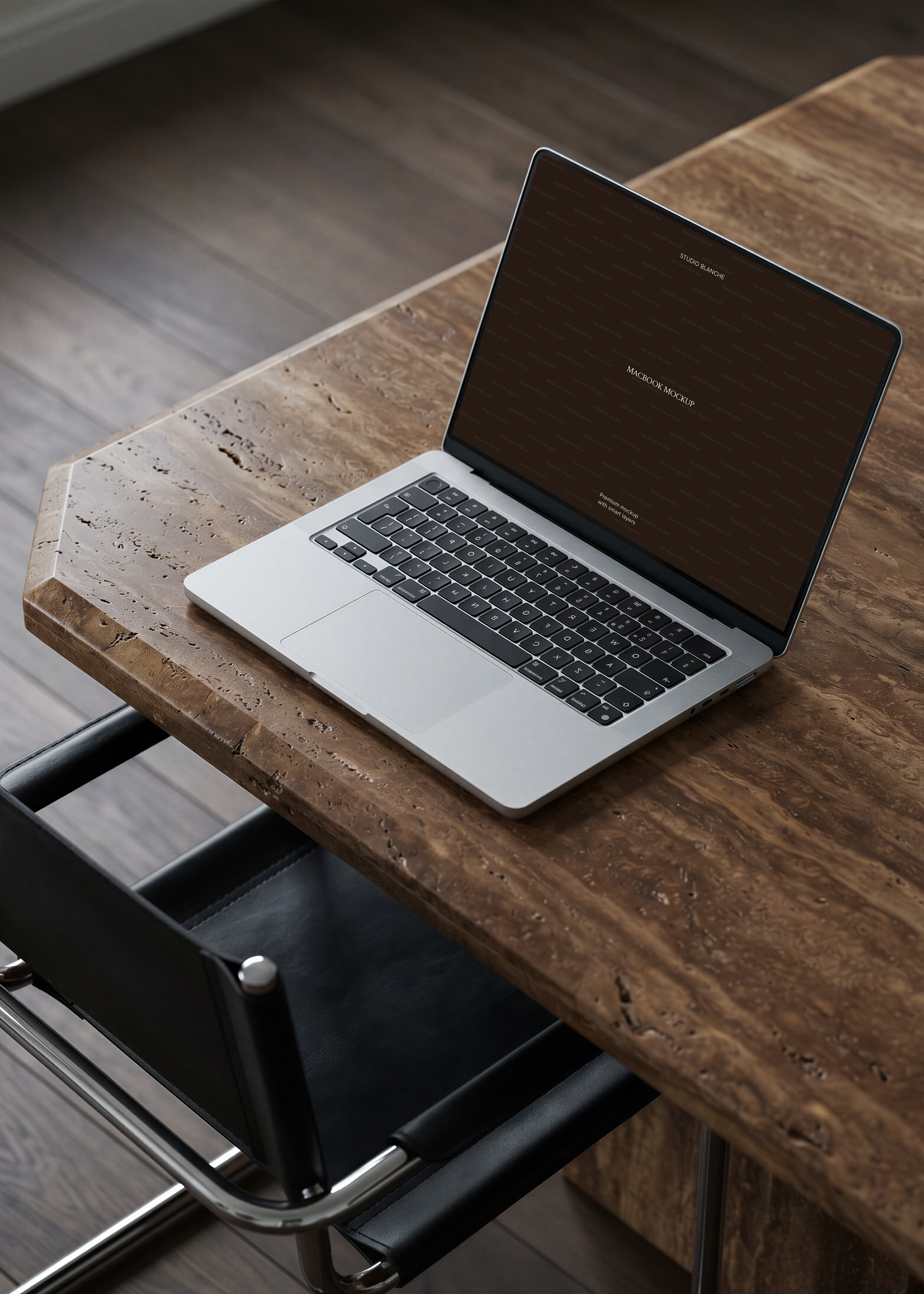 MacBook mockup open on raw travertine desk beside black leather and chrome chair, warm moody editorial office scene