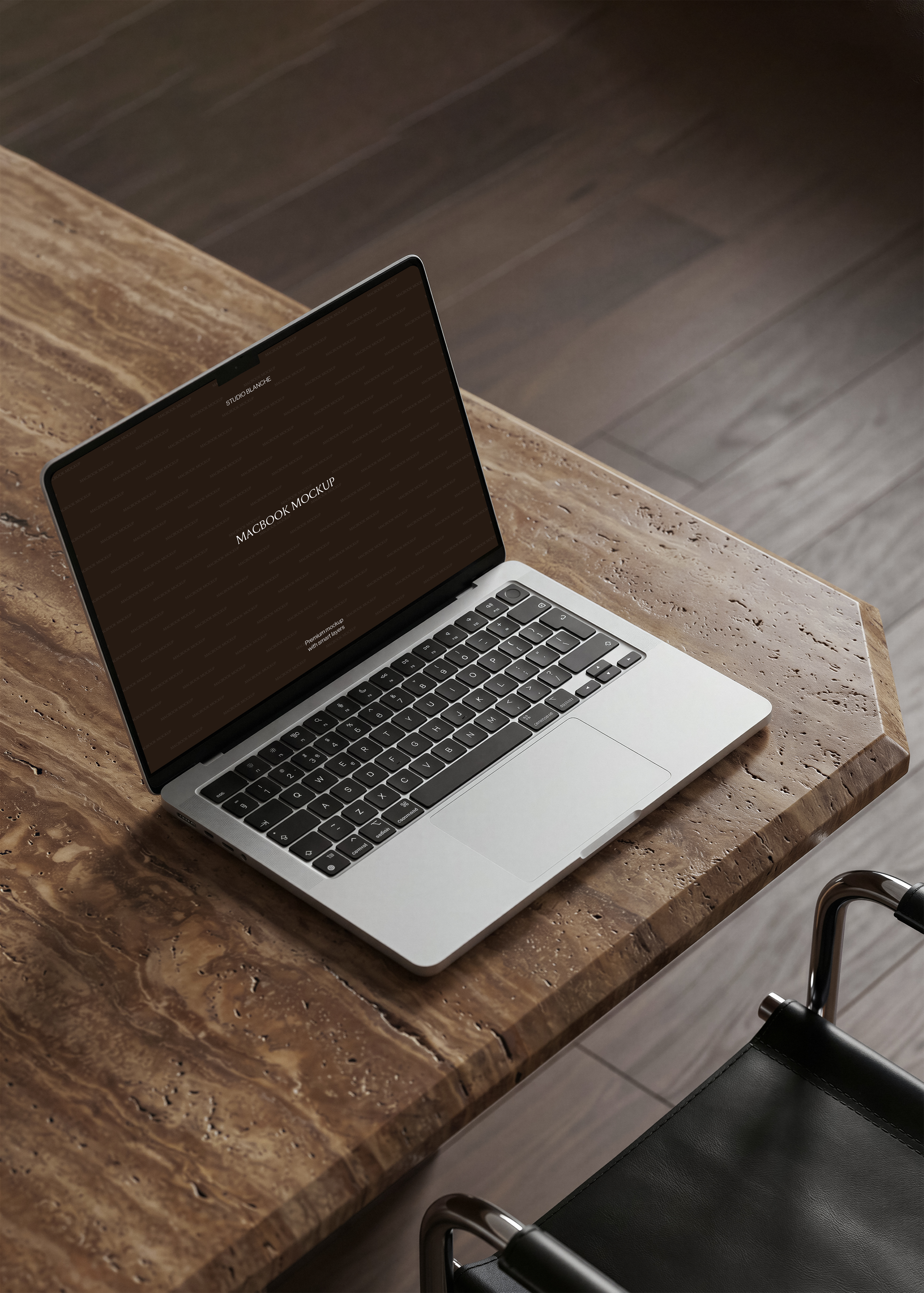 MacBook mockup from overhead on thick travertine desk, dark herringbone oak floor and black leather steel chair corner