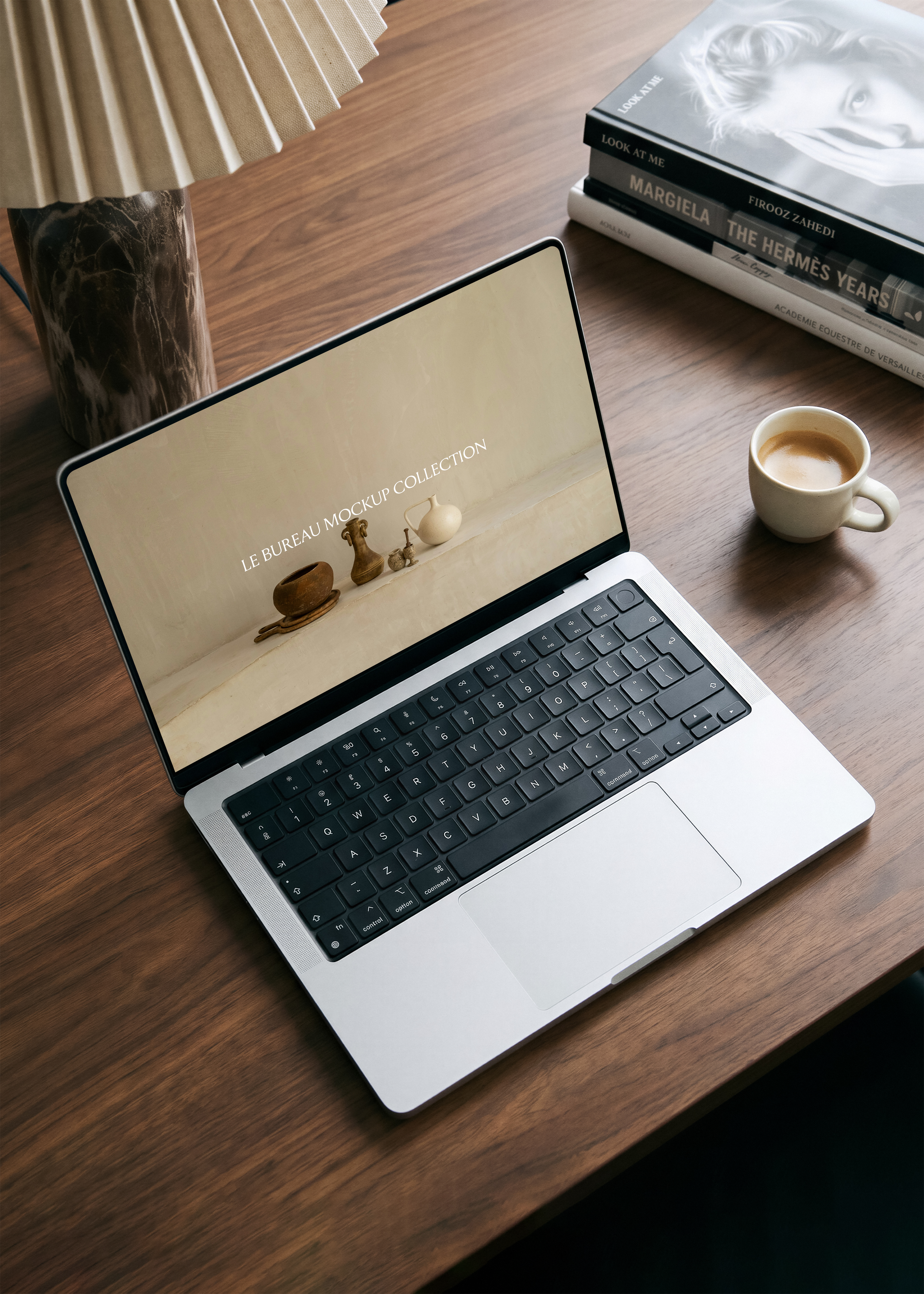 MacBook mockup displaying Le Bureau editorial from overhead on walnut desk, fashion books, espresso and marble vase