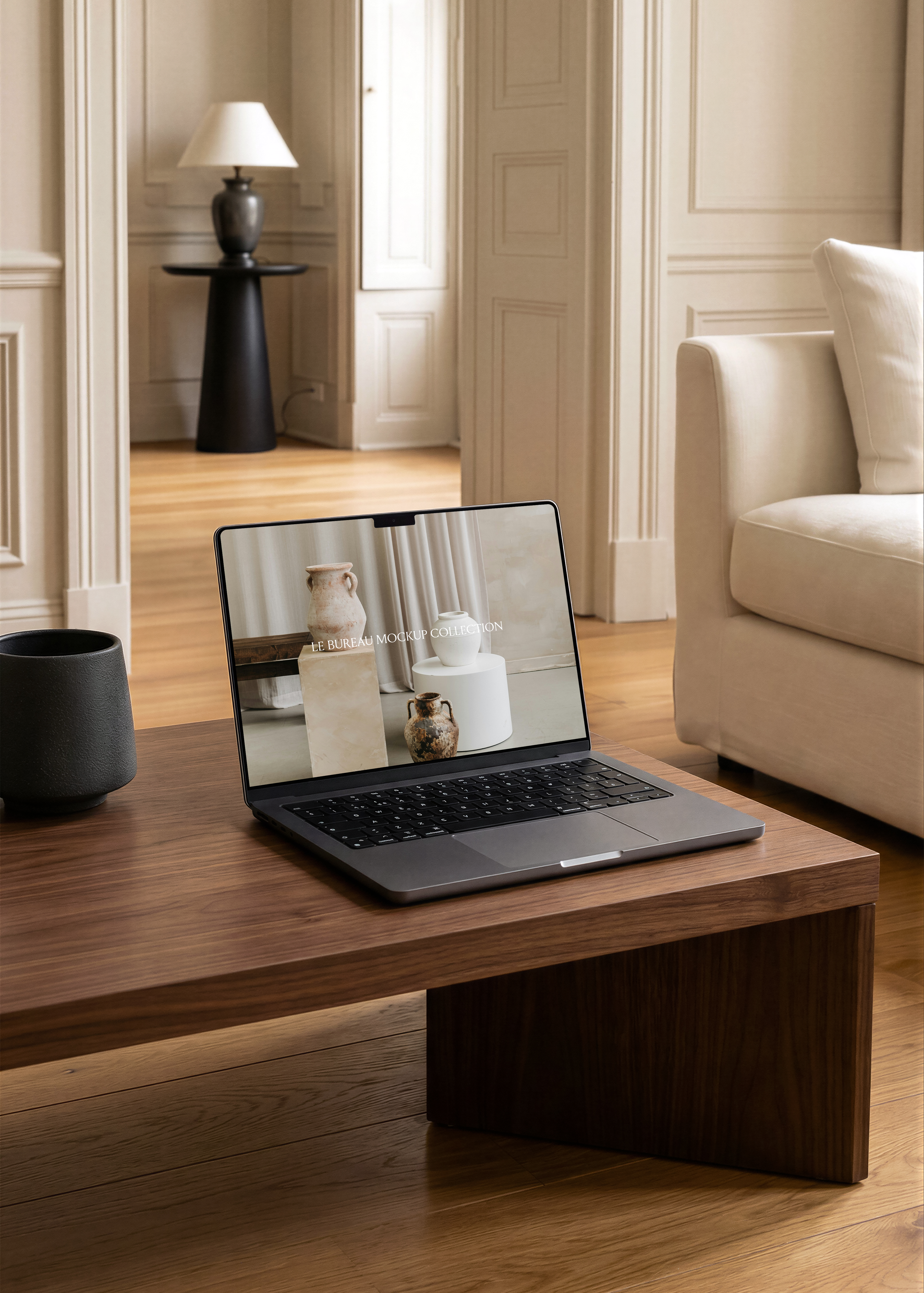 MacBook mockup displaying Le Bureau editorial on walnut coffee table, cream armchair and Parisian moulded interior backdrop