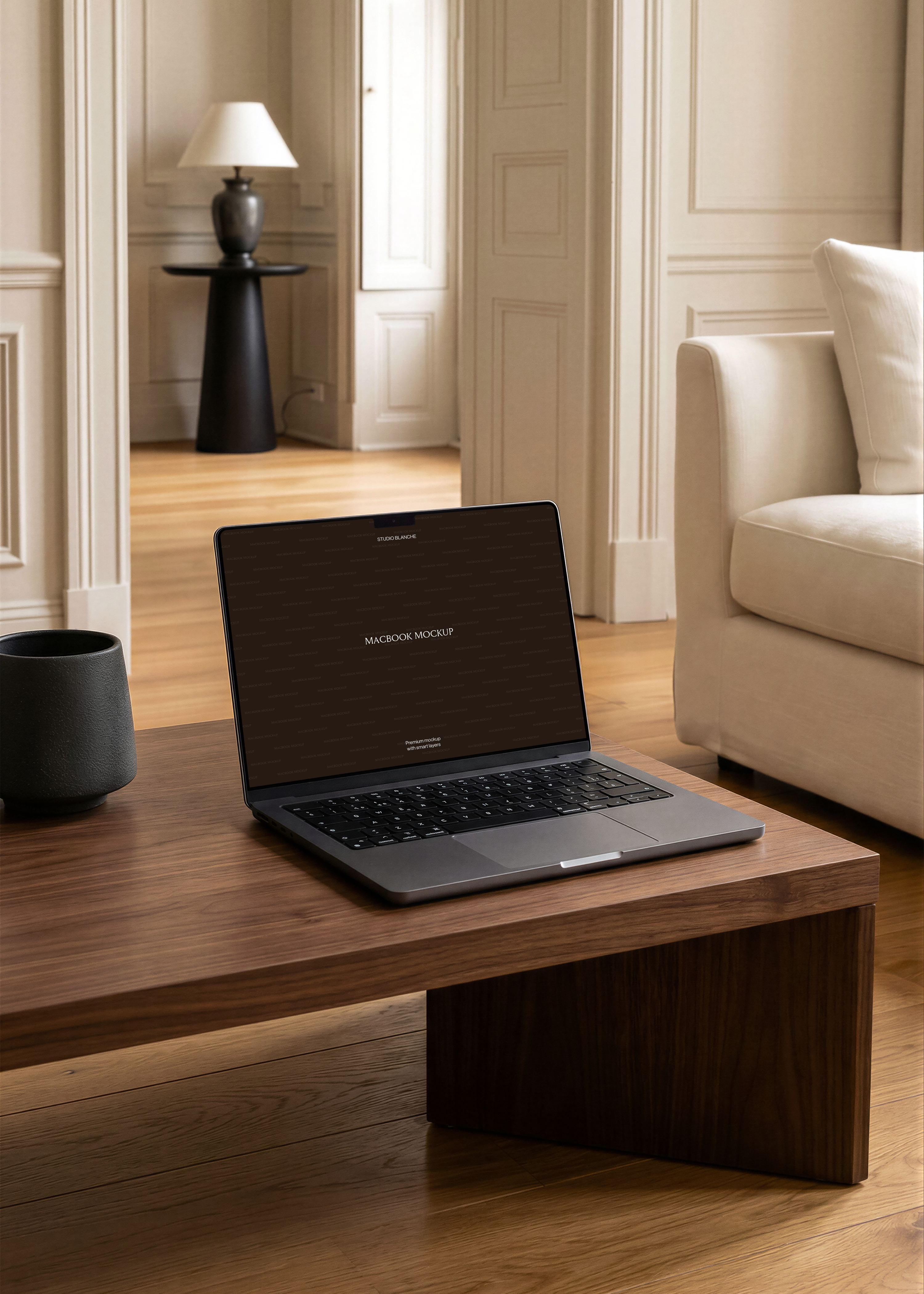 MacBook mockup on dark walnut coffee table, cream armchair, moulded panelling and black lamp visible through doorway
