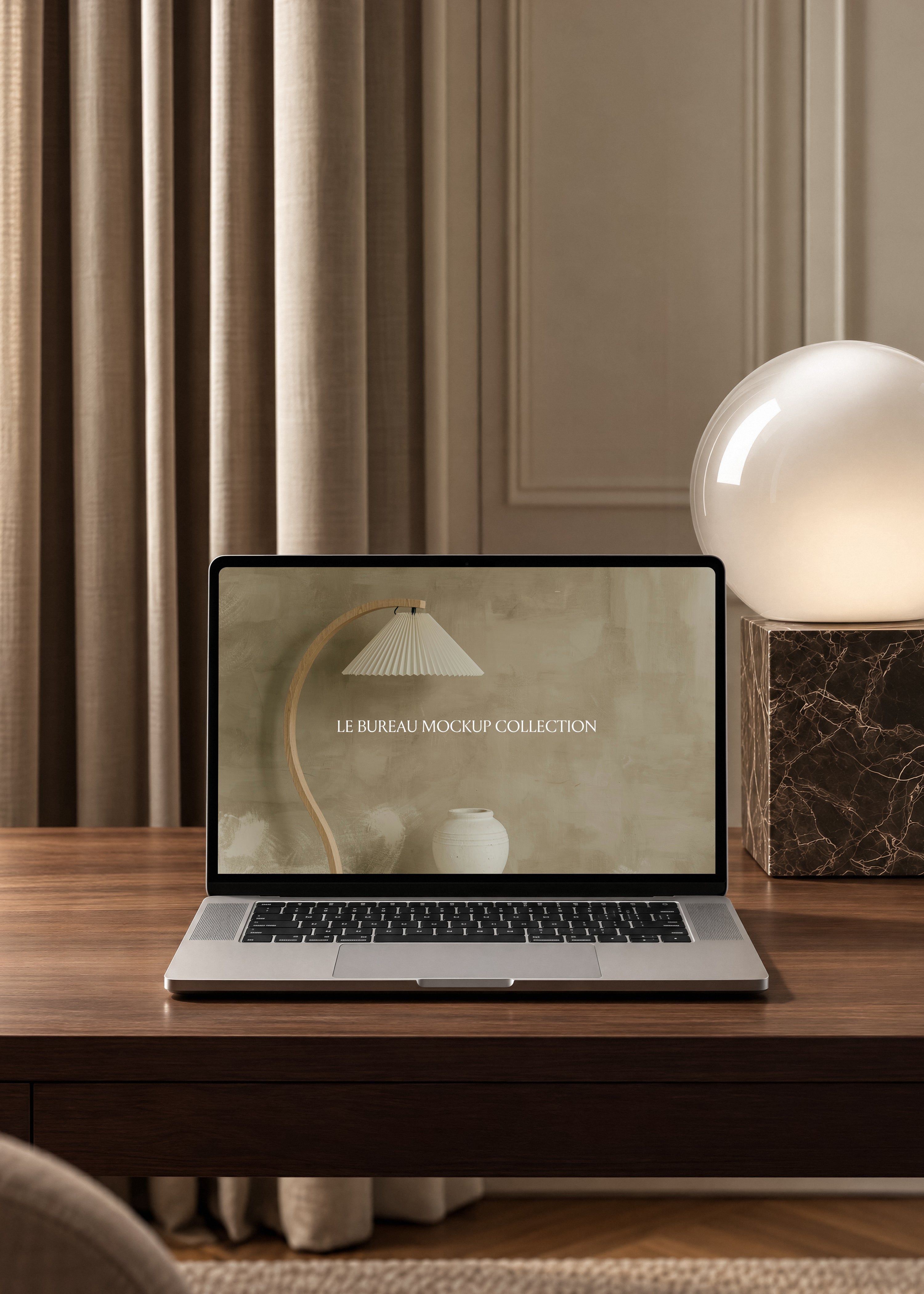 MacBook mockup displaying Le Bureau editorial on oak desk, marble block globe lamp and pleated curtain background