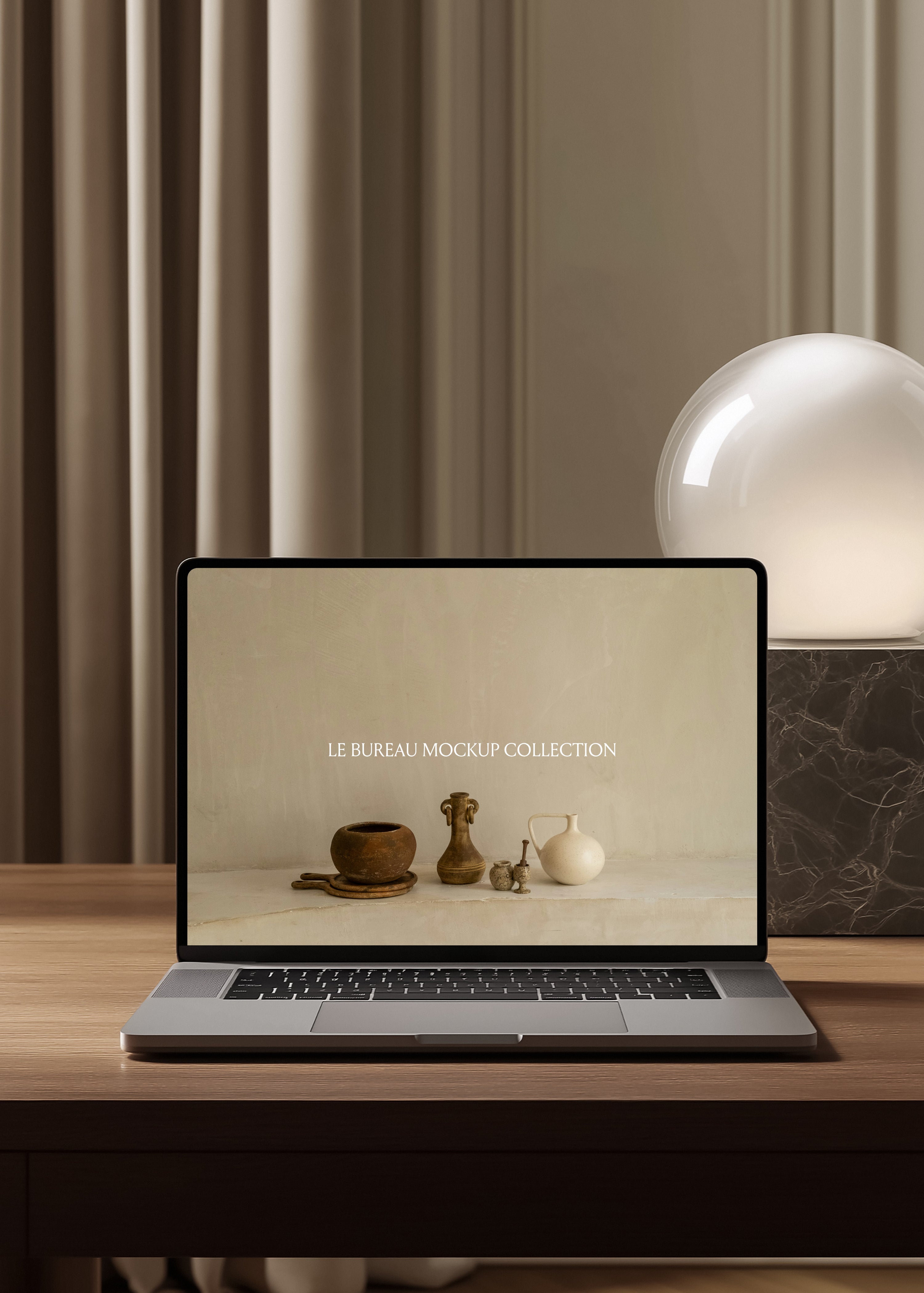 MacBook mockup displaying Le Bureau editorial on oak desk, marble block globe lamp and pleated curtain background