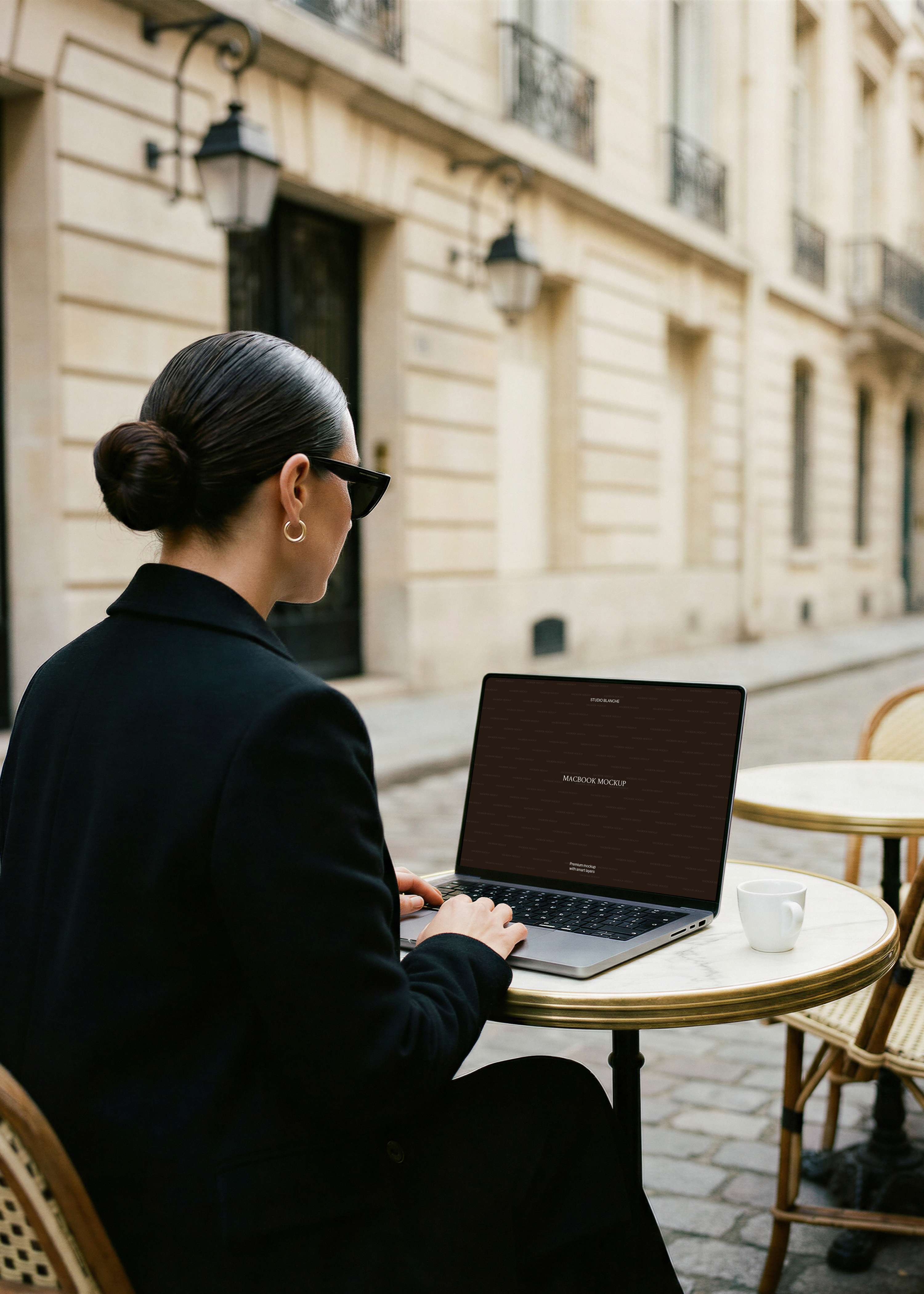 MacBook mockup at Parisian street café, dark editorial screen design, marble bistro table, cobbled street