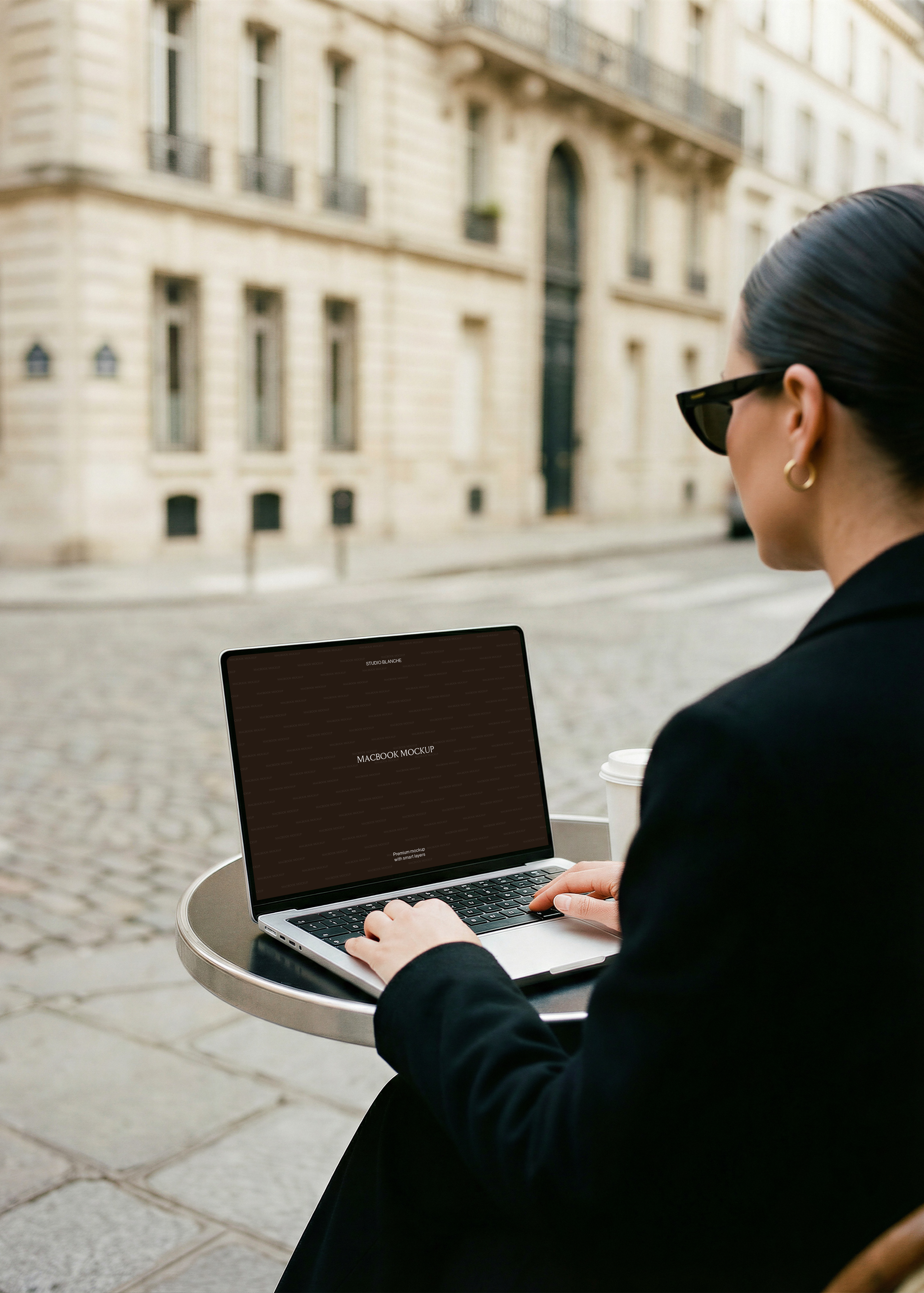 MacBook mockup at open-air Paris café table, dark placeholder screen, Haussmann stone buildings behind
