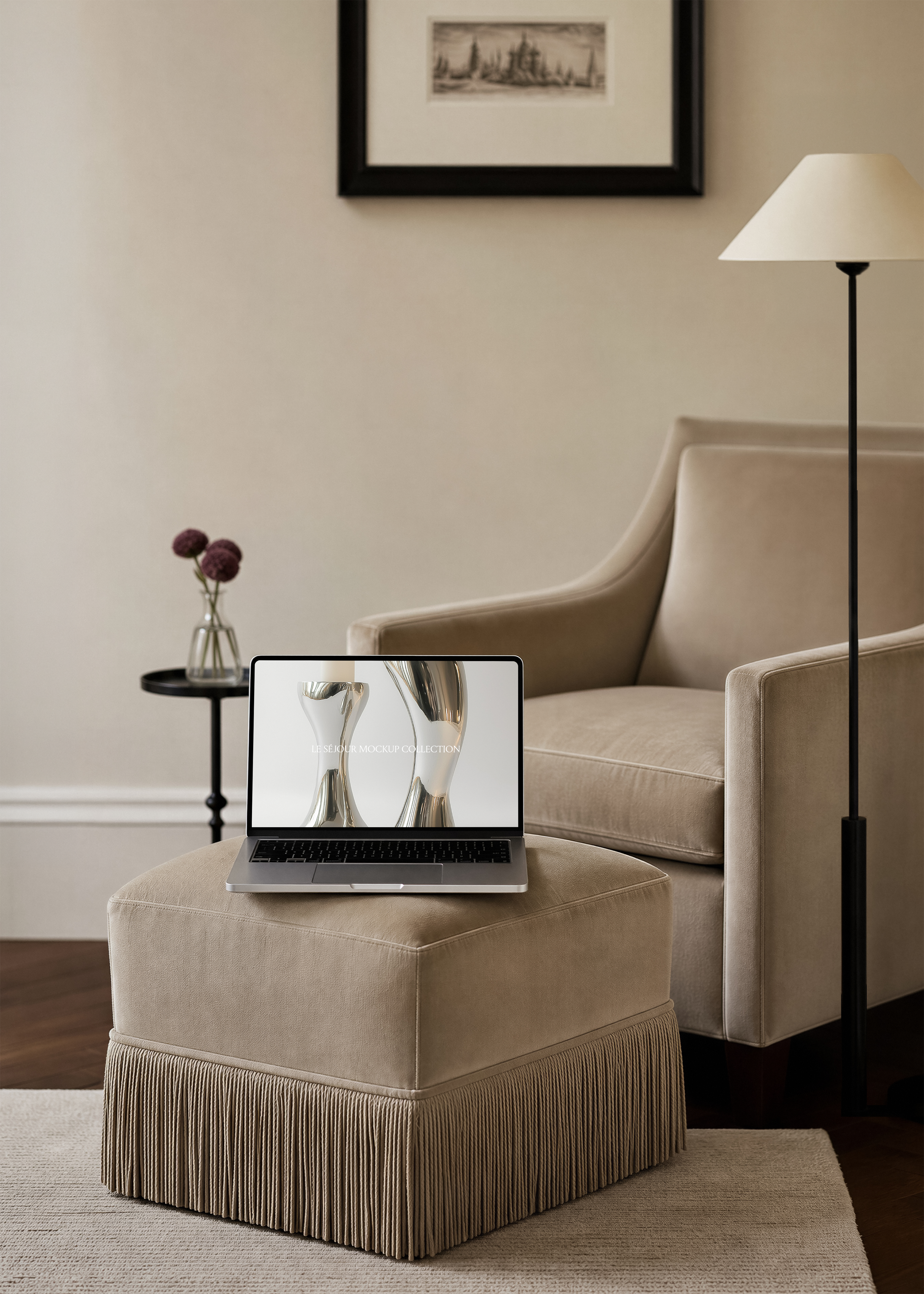 Open MacBook mockup on a taupe velvet fringed ottoman beside a velvet armchair, black floor lamp and framed print behind
