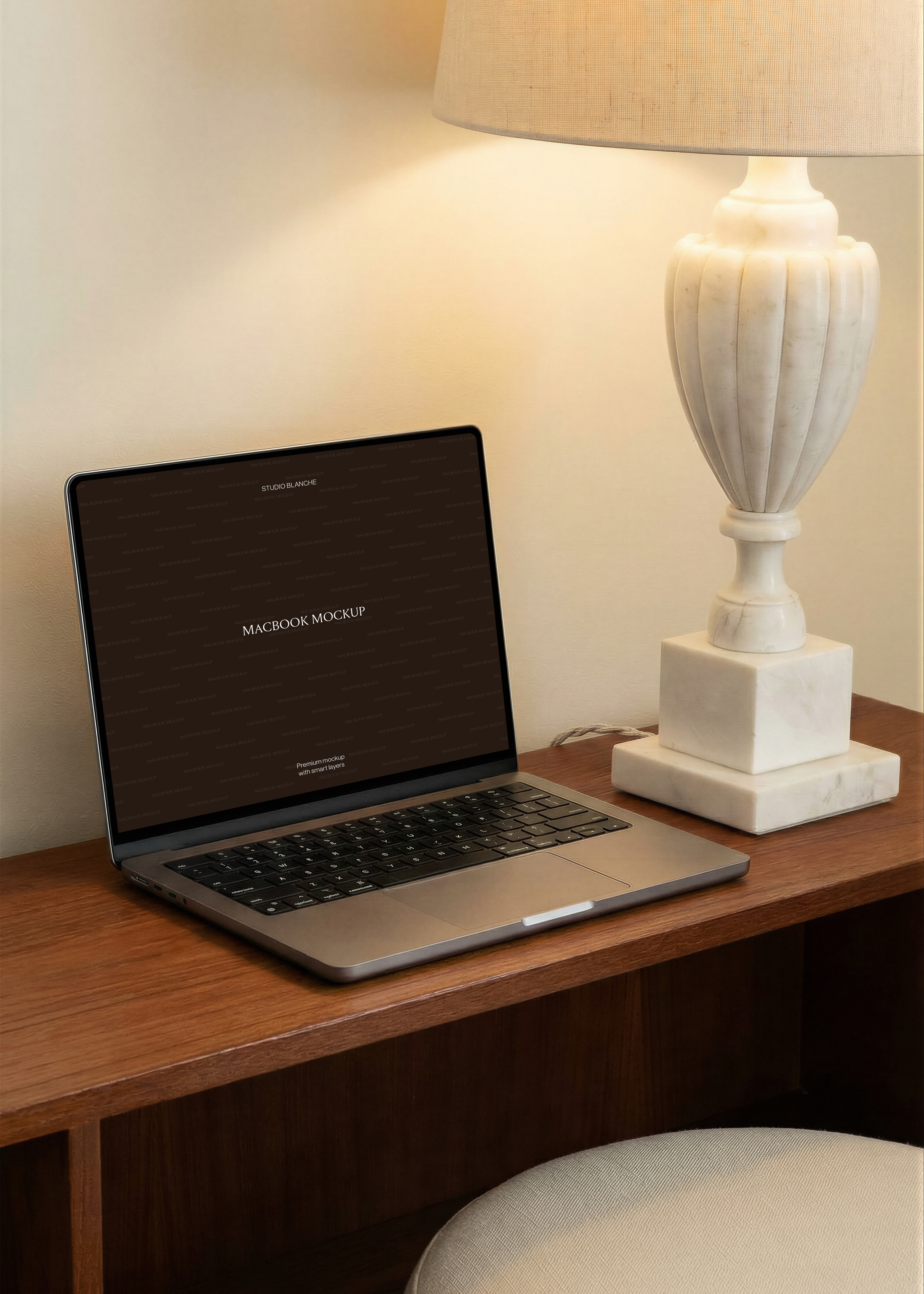 MacBook mockup on warm walnut console beside carved white marble urn lamp with wide linen drum shade, cream wall interior