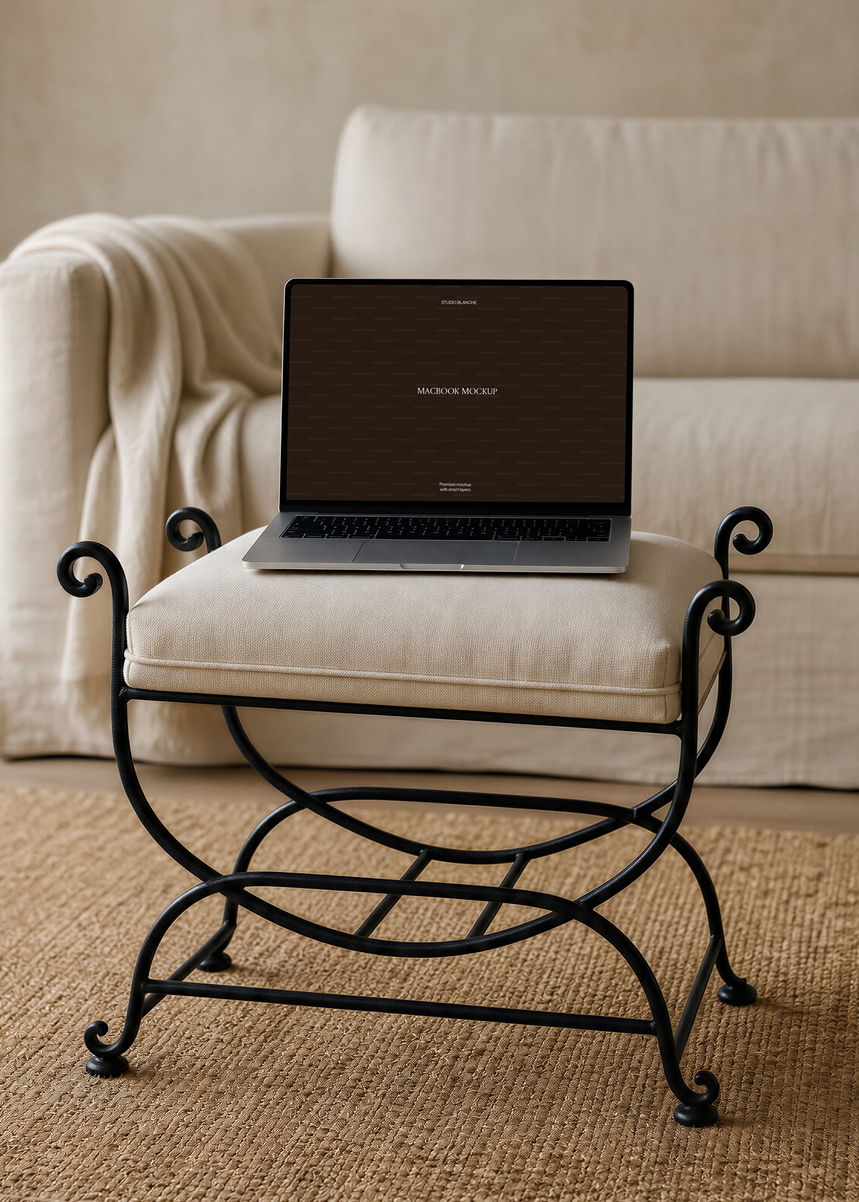MacBook mockup detail of a dark laptop screen on a cream linen cushion framed by black scrolled iron arms, linen sofa behind