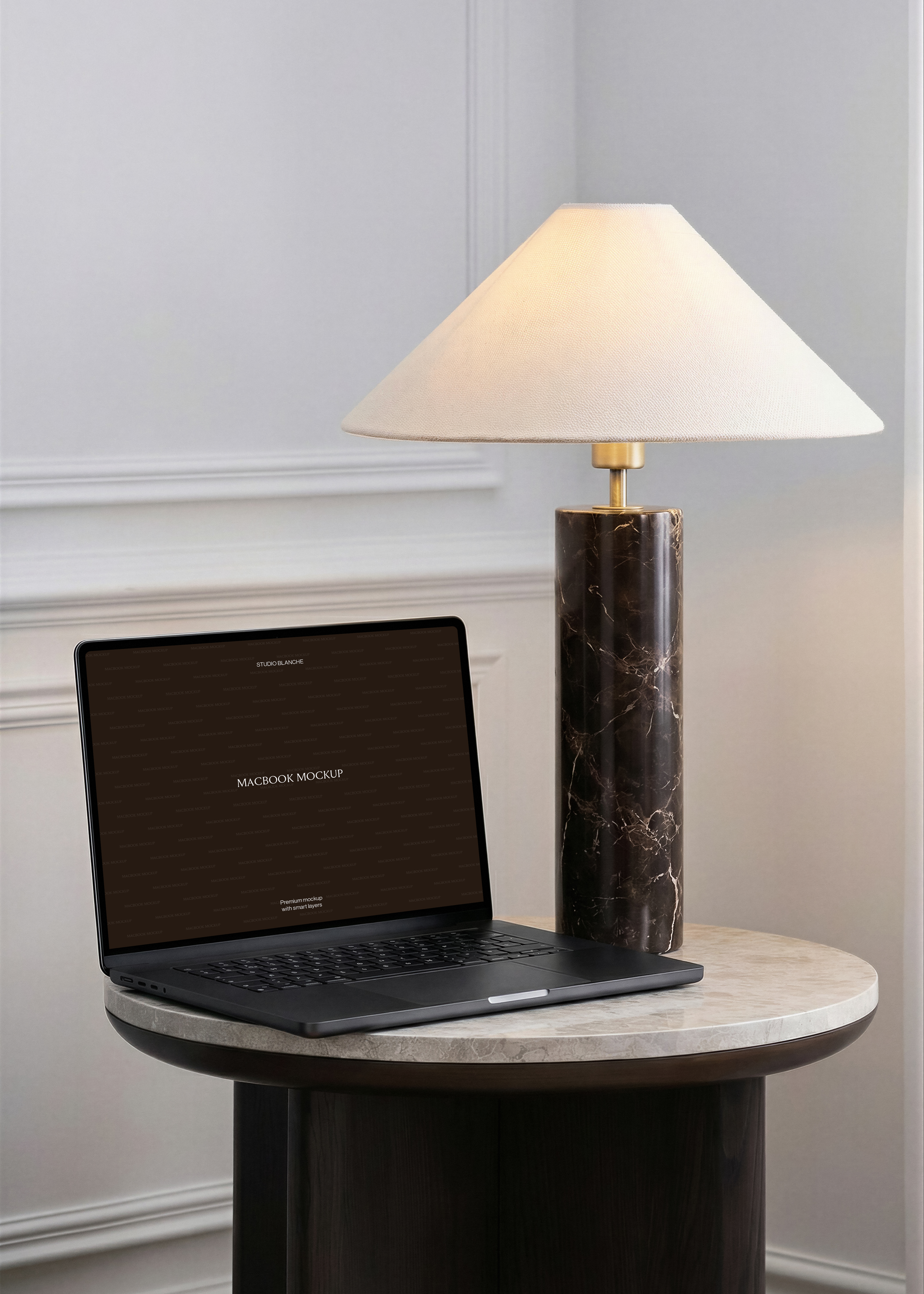 MacBook mockup on marble side table beside dark veined marble column lamp, brass fitting and cream shade, grey panelled wall
