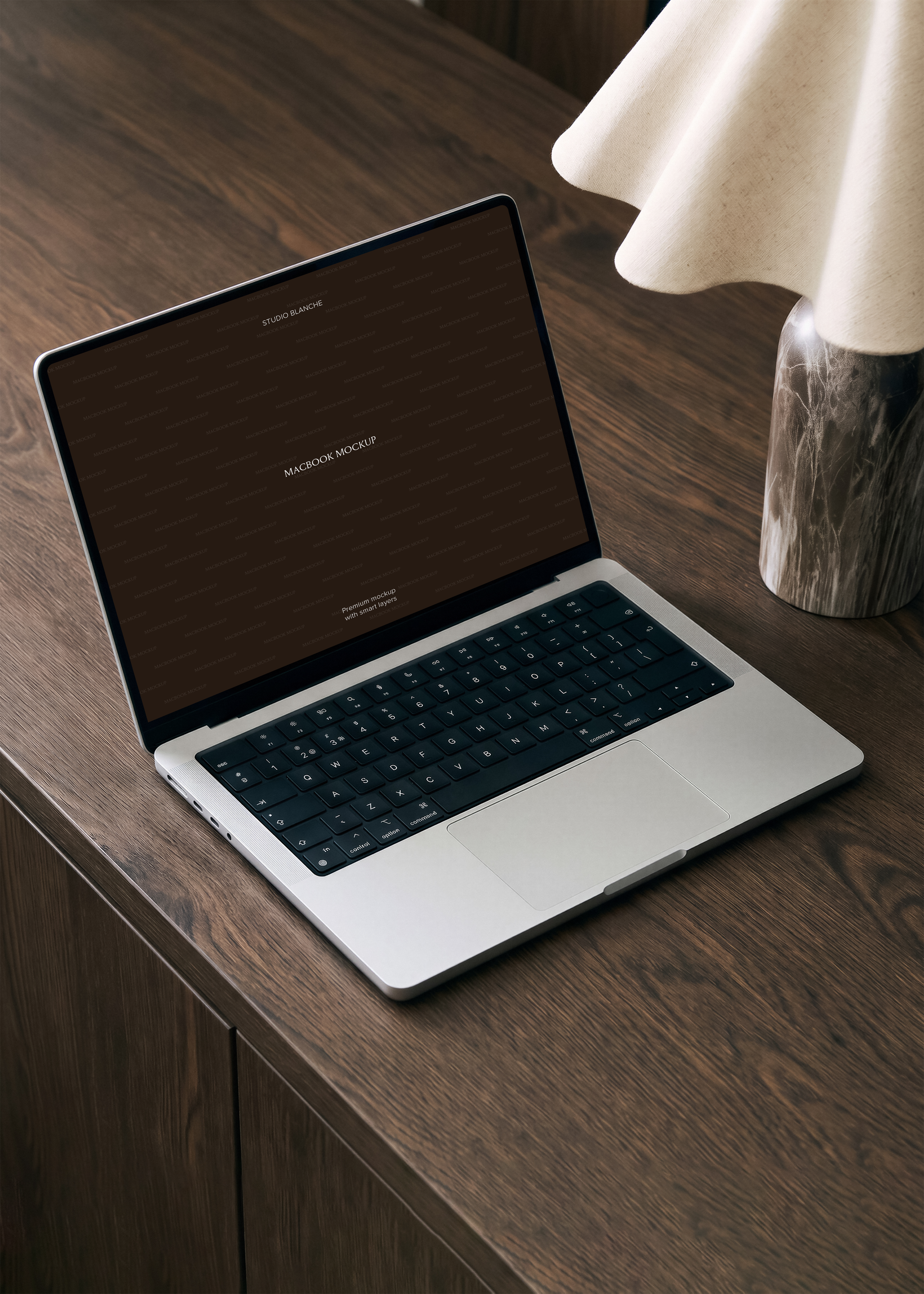MacBook mockup open on dark walnut desk beside sculptural marble-base lamp, warm moody editorial office scene