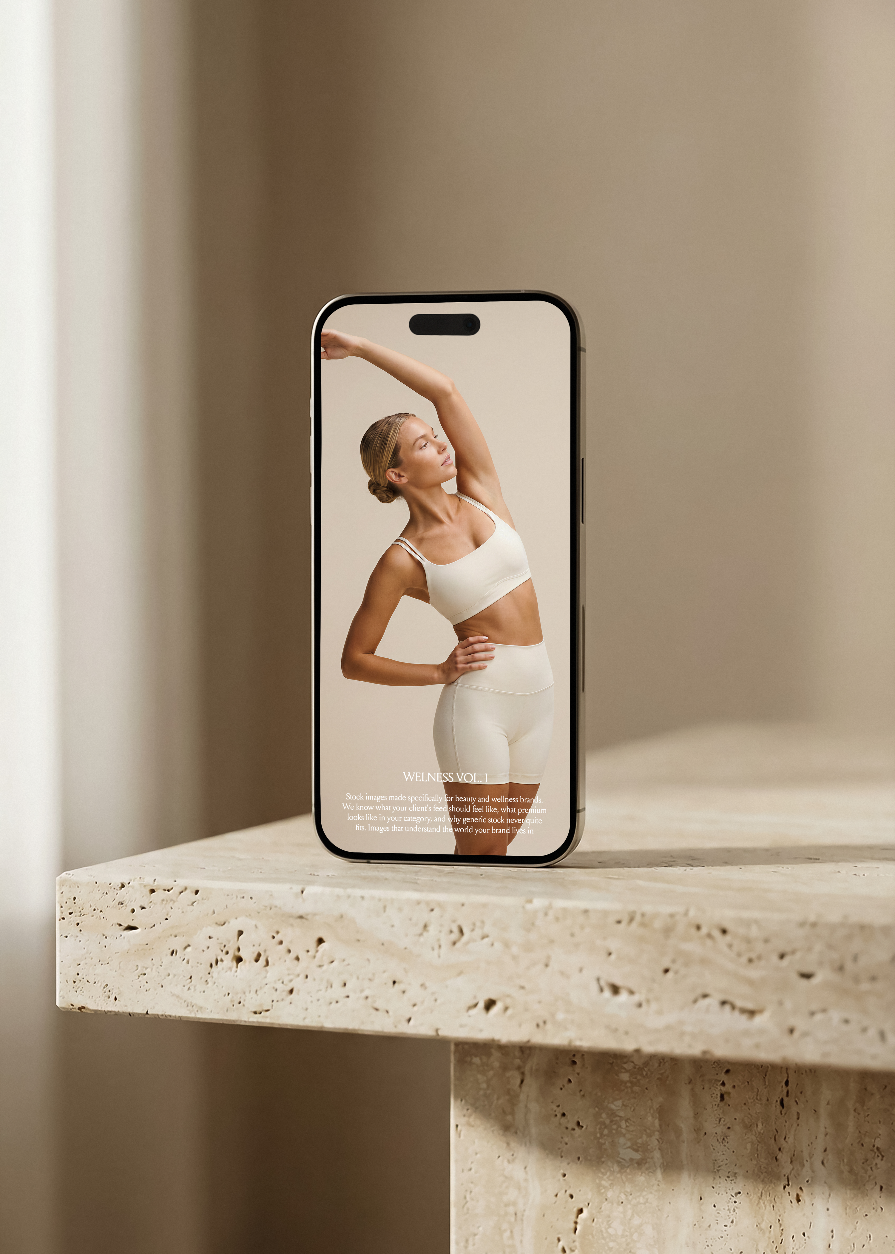 iPhone mockup on travertine surface displaying Wellness Vol. I editorial stock image, woman in white activewear stretching, warm neutral tones