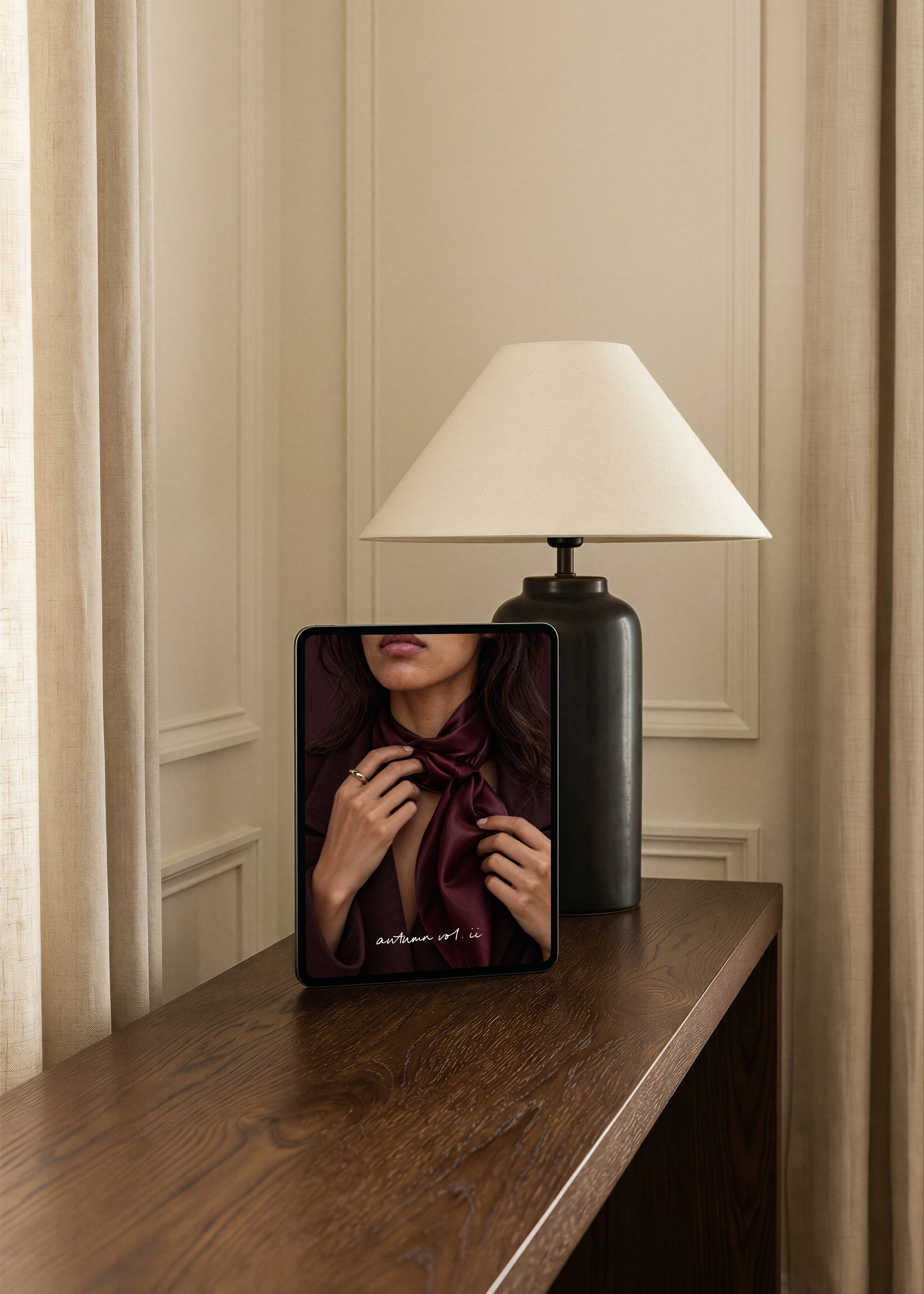 Tablet showing a burgundy silk scarf photo beside a dark ceramic lamp on an oak sideboard, Studio Blanche