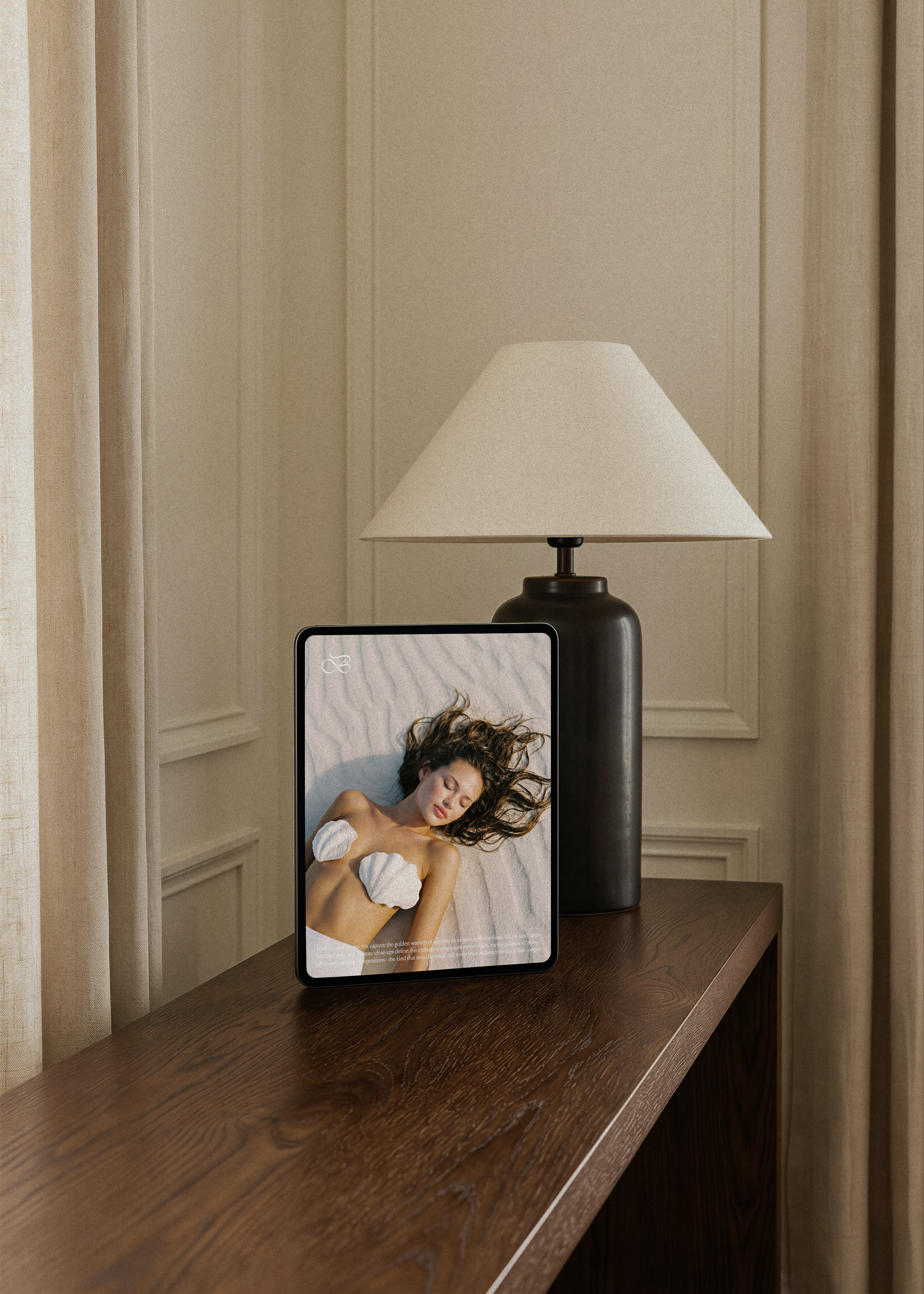Summer stock collection shown on tablet screen on dark wood console beside a black lamp, warm coastal editorial styling